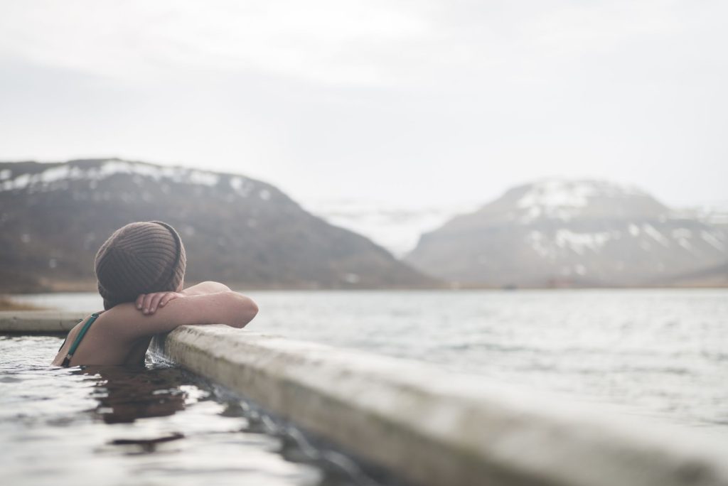 Person relaxing in outdoor pool with mountainous backdrop. Winter serenity.