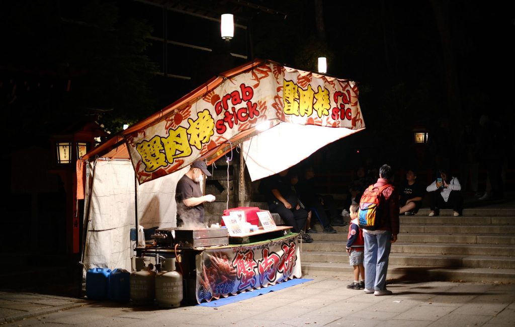 A vibrant street food stall at night selling crab sticks with customers visiting.