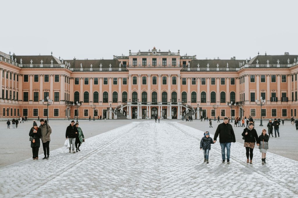 People walking in the courtyard of Schonbrunn Palace in Vienna, showcasing baroque architecture.