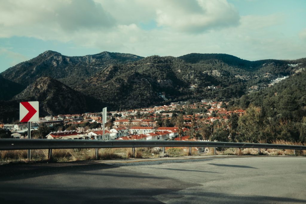 A picturesque view of a small town nestled in lush mountains taken from a roadside vantage point.