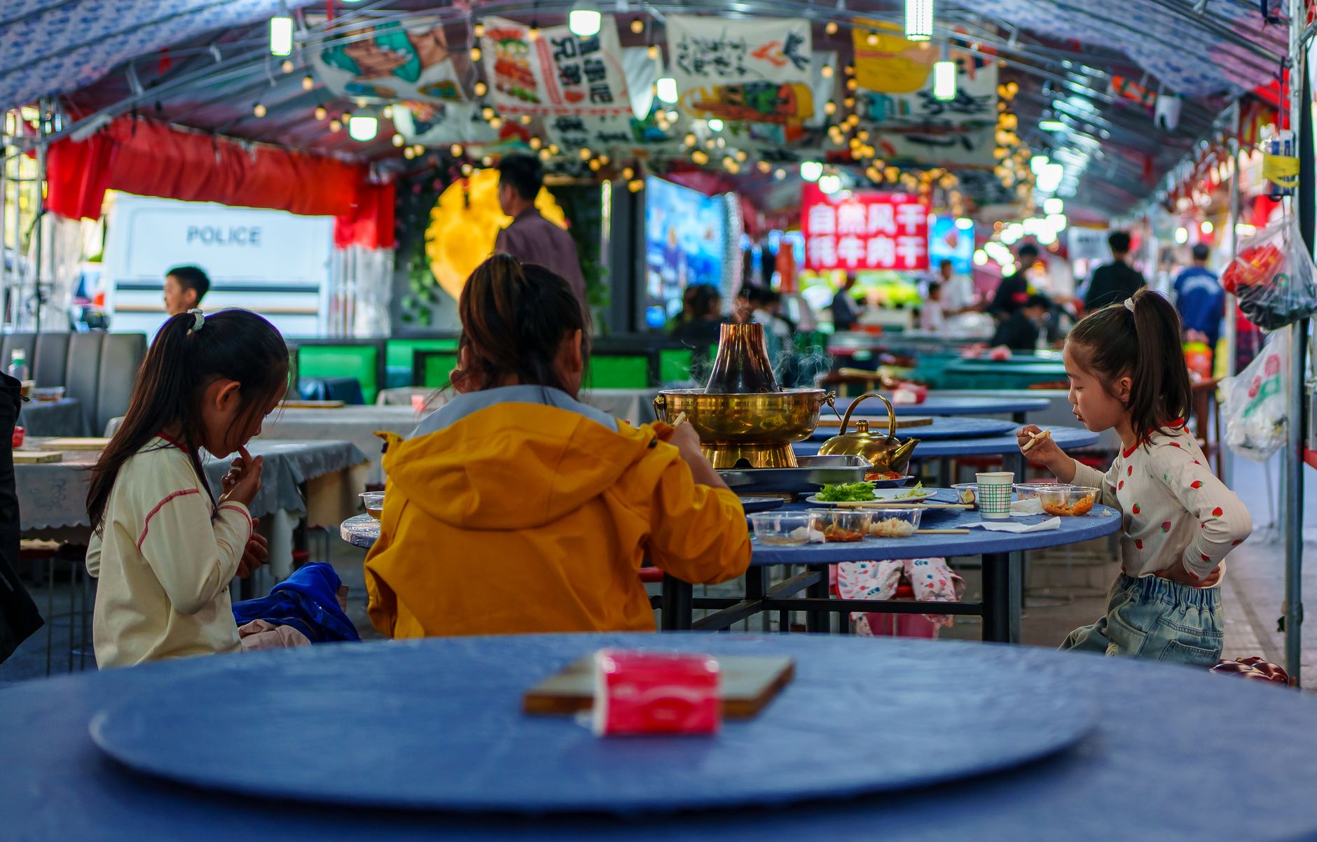Children dining at a colorful street market in Qinghai, China, showcasing vibrant culture and traditional cuisine.