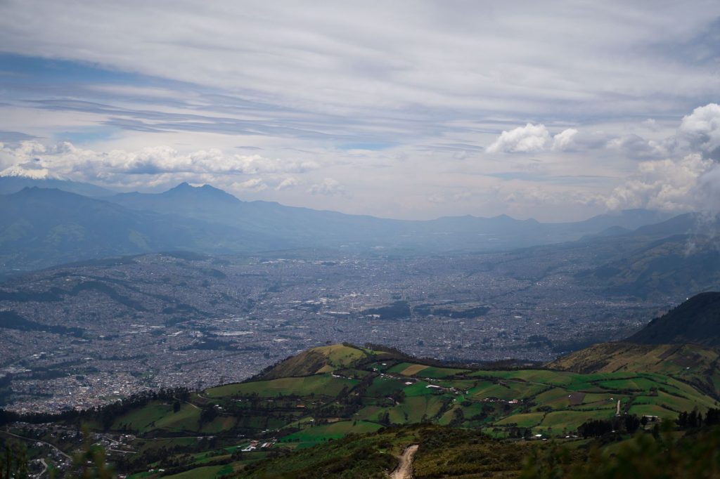 A breathtaking aerial shot of Quito, displaying lush valleys and rugged mountains under a dynamic sky.