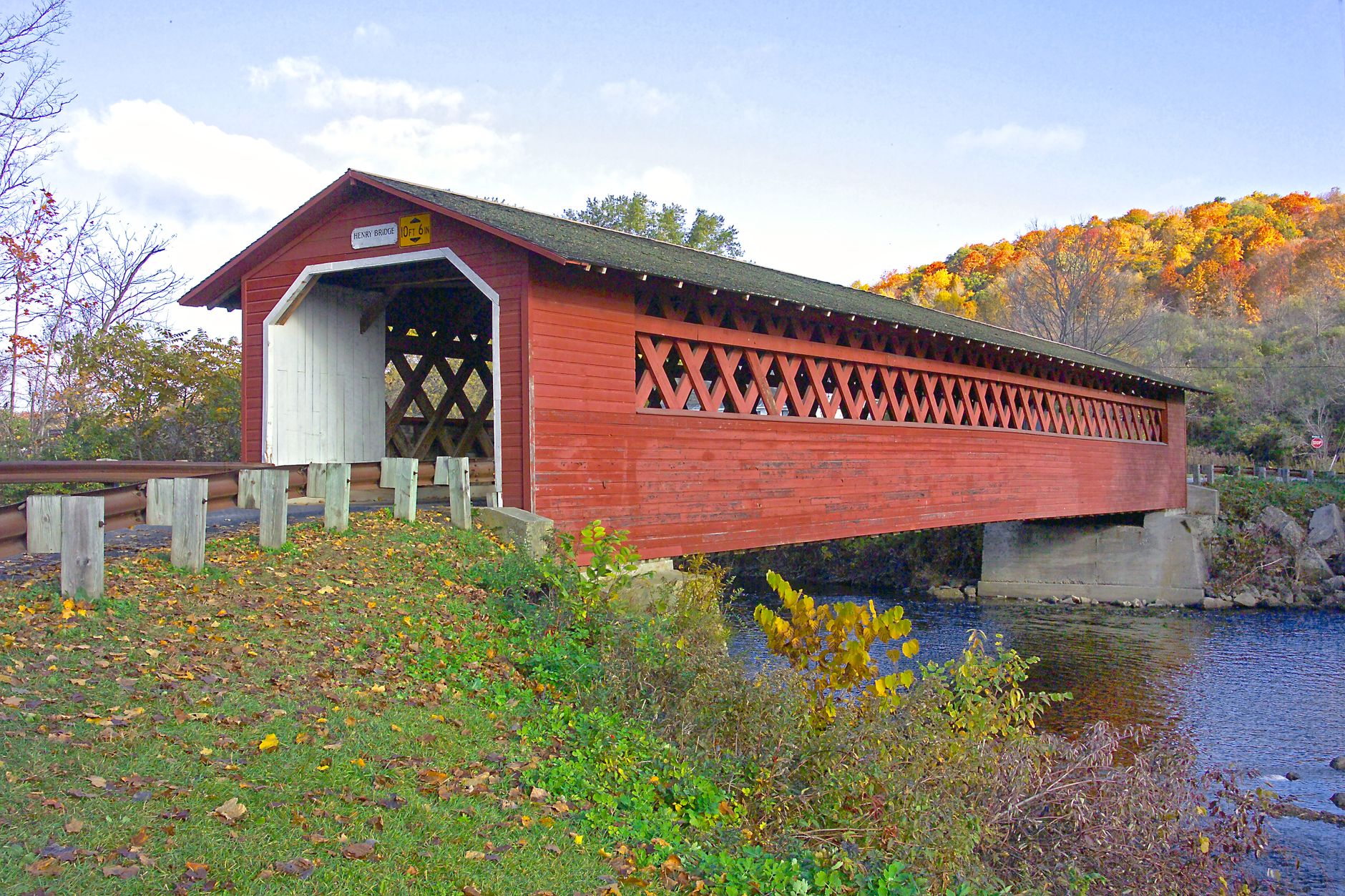 Red covered bridge over a river in Vermont surrounded by vibrant fall foliage, showcasing classic wooden architecture.