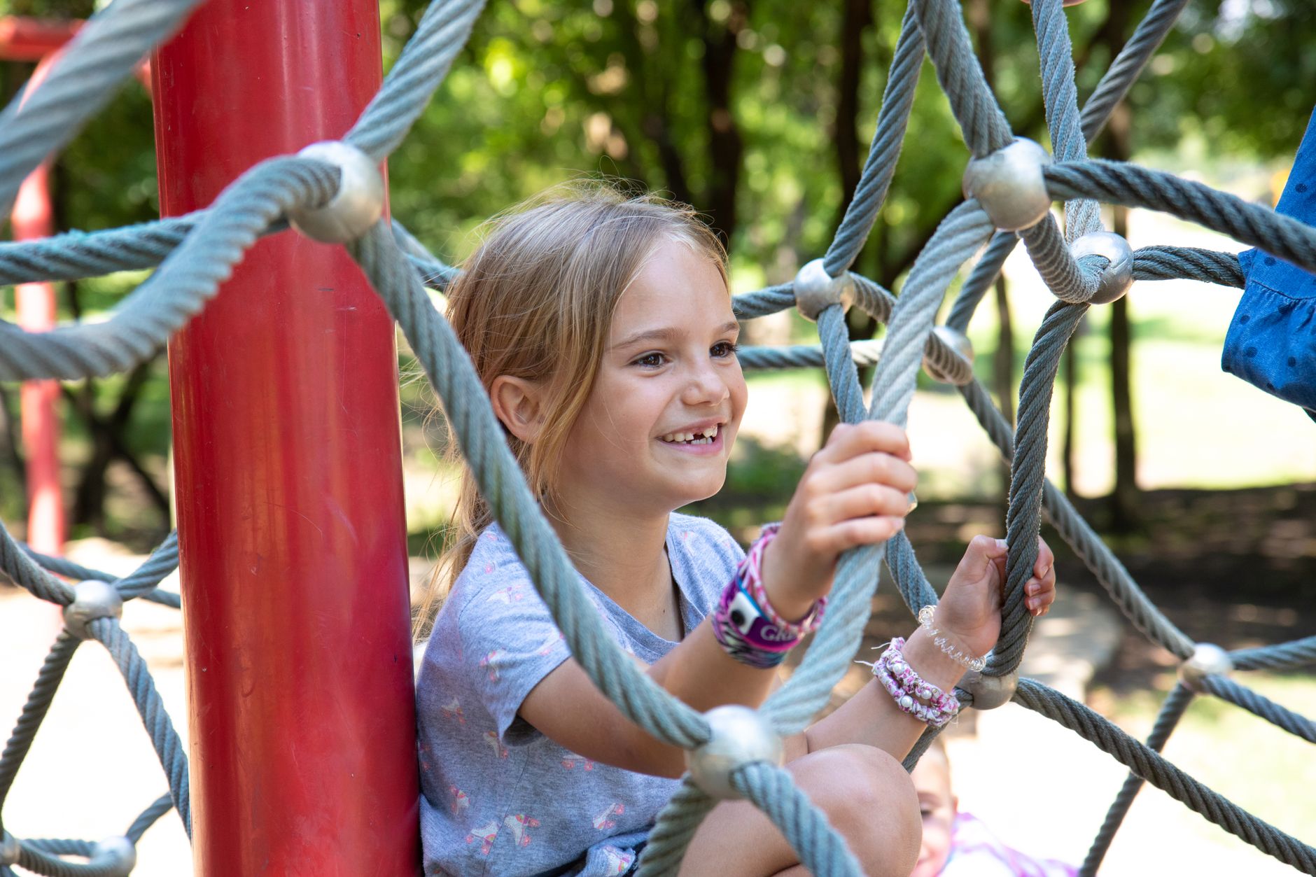 Happy young girl climbing on a rope structure in an outdoor playground, enjoying a sunny day.