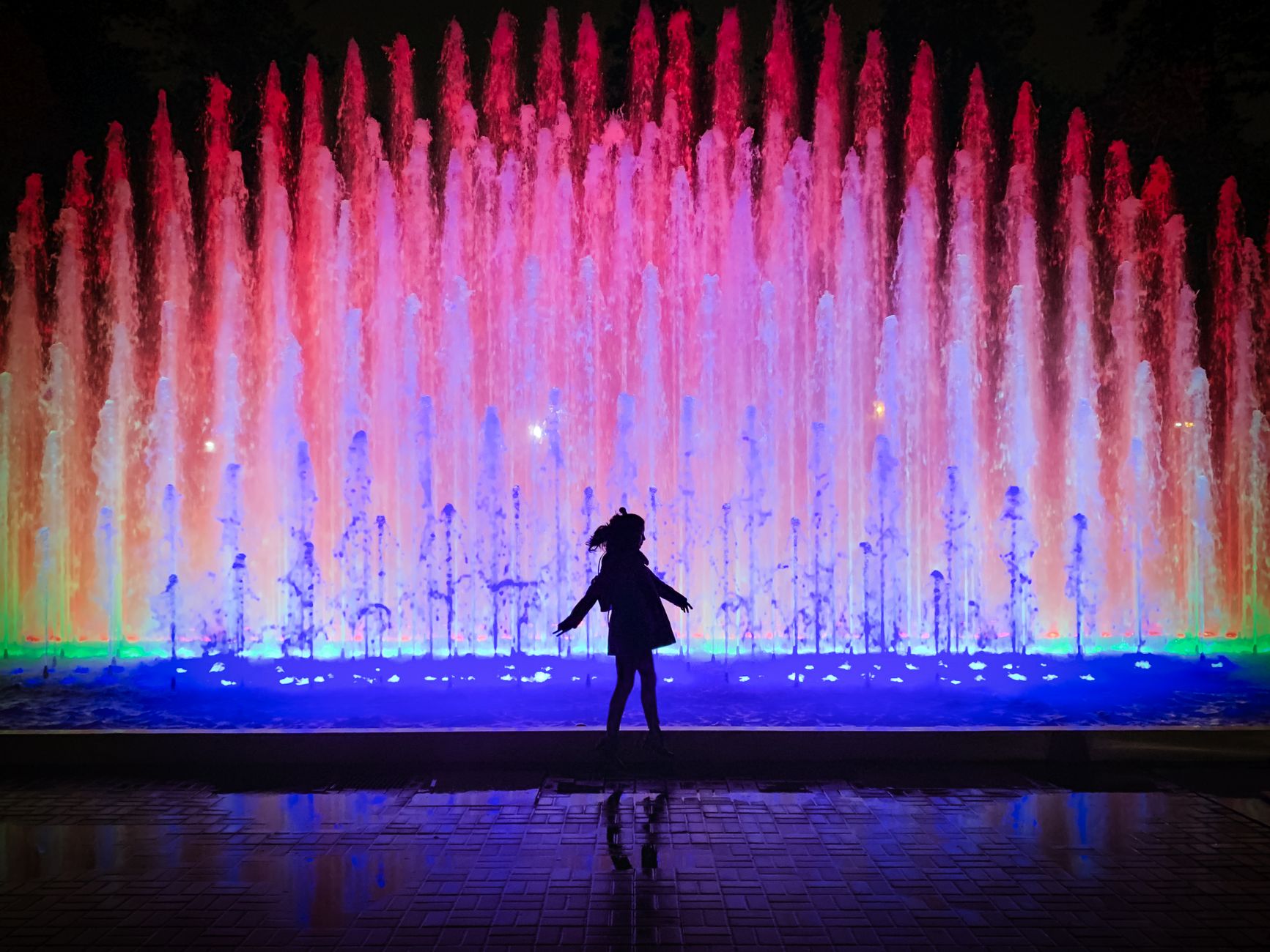 Silhouette of a person in front of colorful illuminated fountains at Lima's Magic Water Circuit.