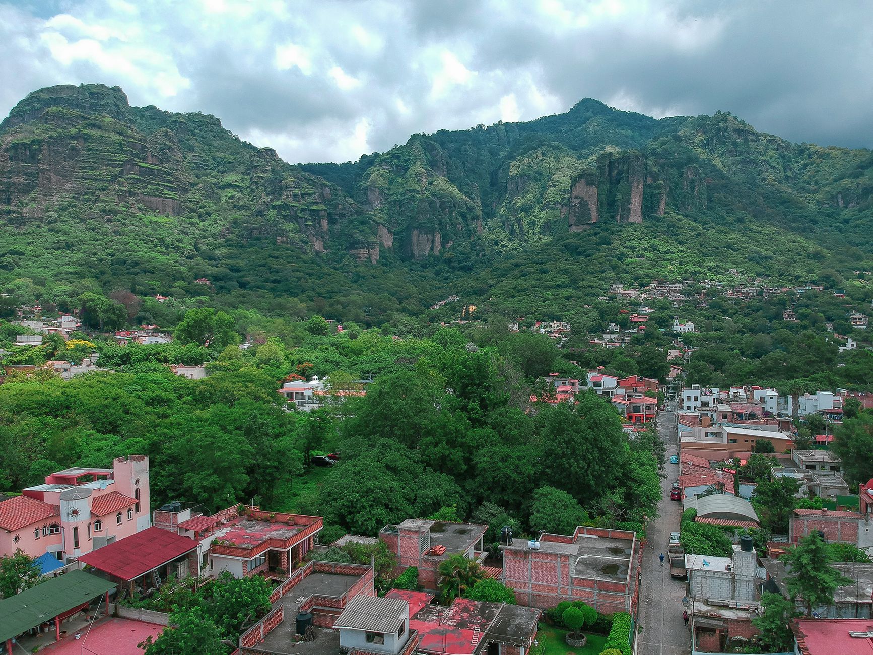 Scenic aerial view of Tepoztlán town with lush green mountains and cloudy sky in the background.