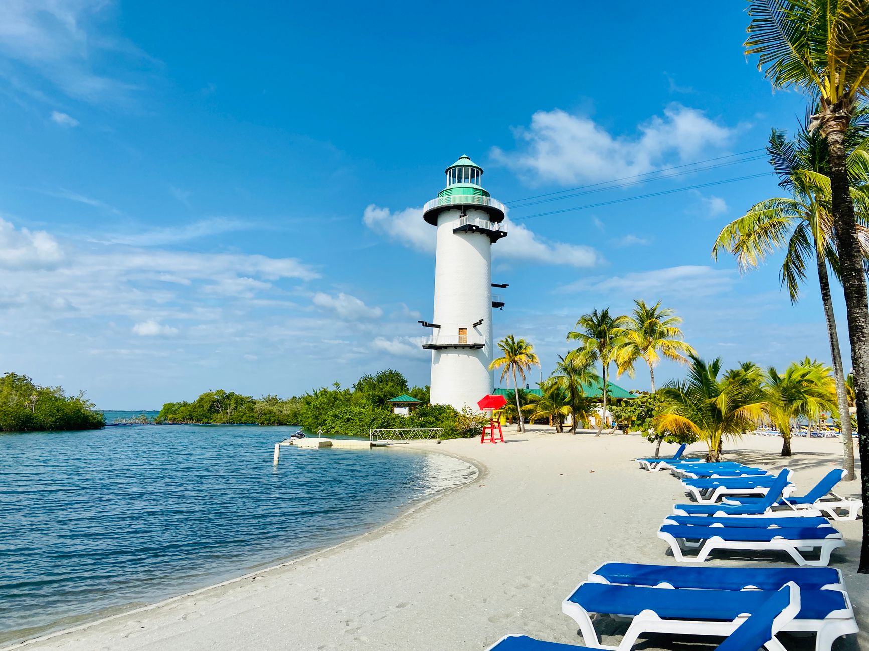 Serene beach scene with a white lighthouse and palm trees under a bright blue sky in Belize.