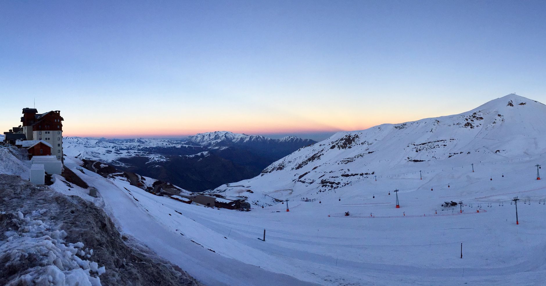 A stunning snowy mountain landscape during sunset in Lo Barnechea, Chile, showcasing ski slopes and scenic views.