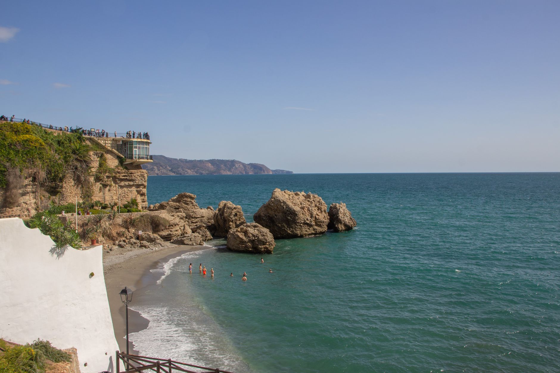 A stunning view of Nerja's Balcon de Europa with beachgoers and rocky sea shore.