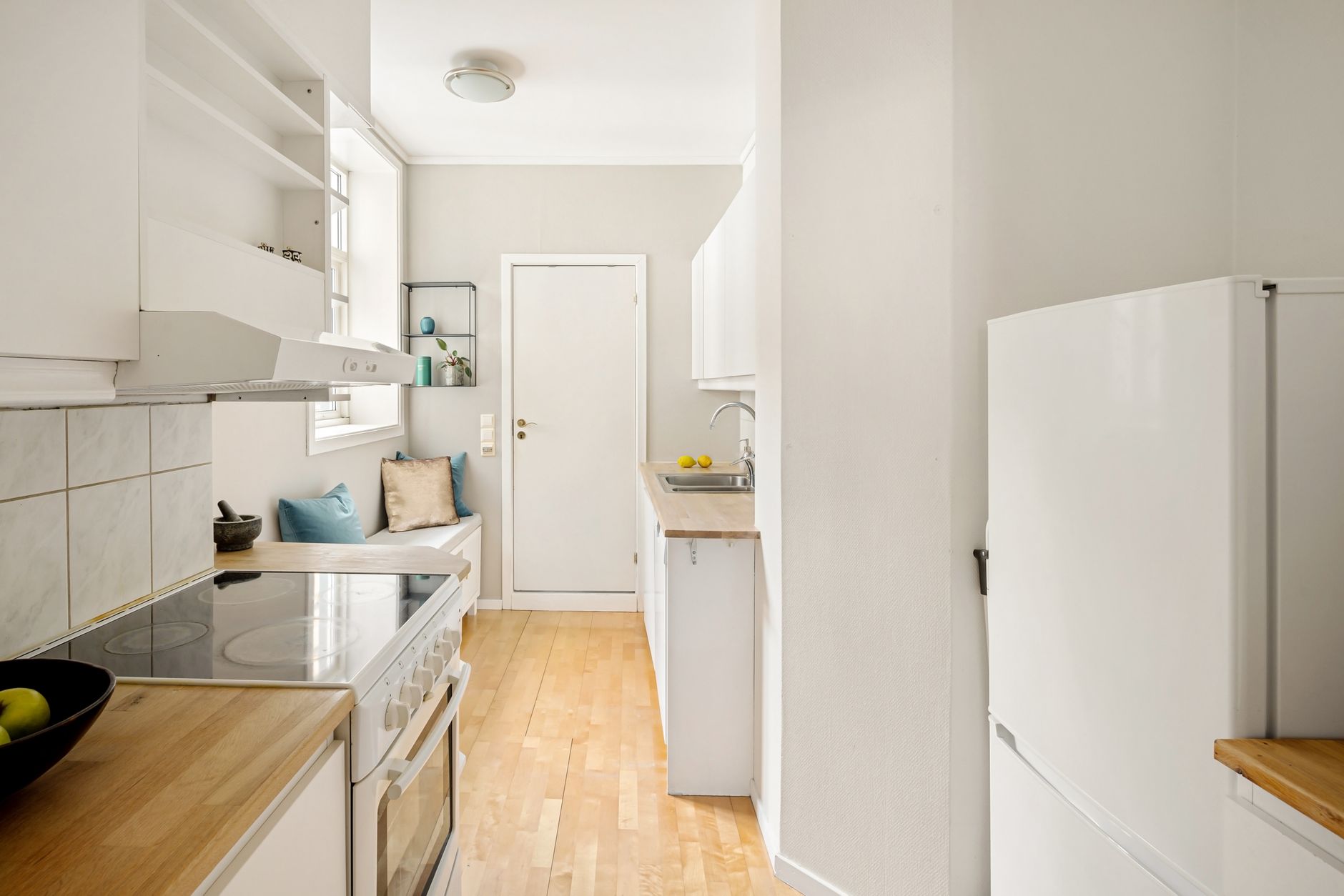 Modern white kitchen with wooden floors and minimalistic design, featuring a cozy seating area.