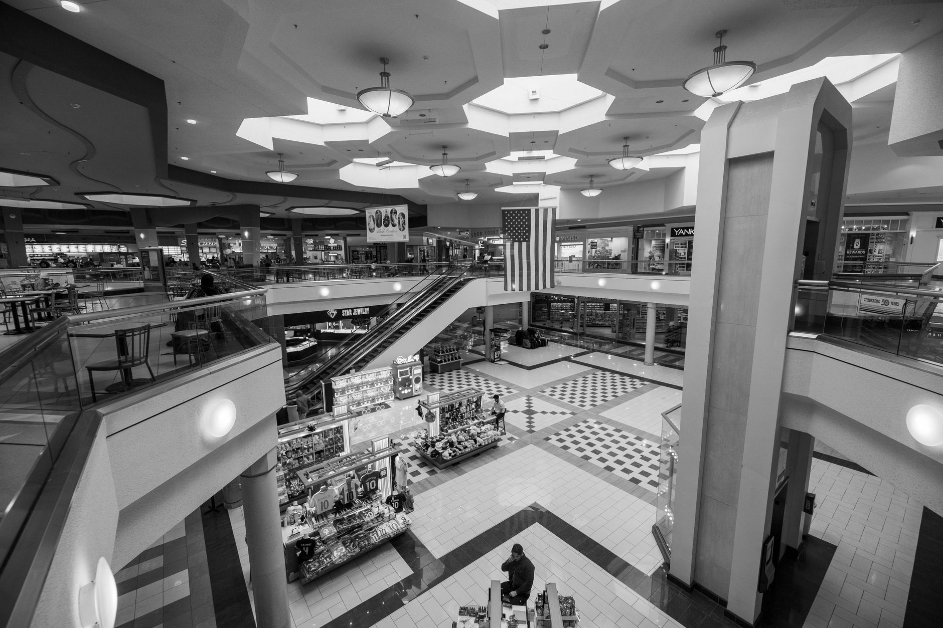 A spacious, modern indoor shopping mall with escalators and an American flag.