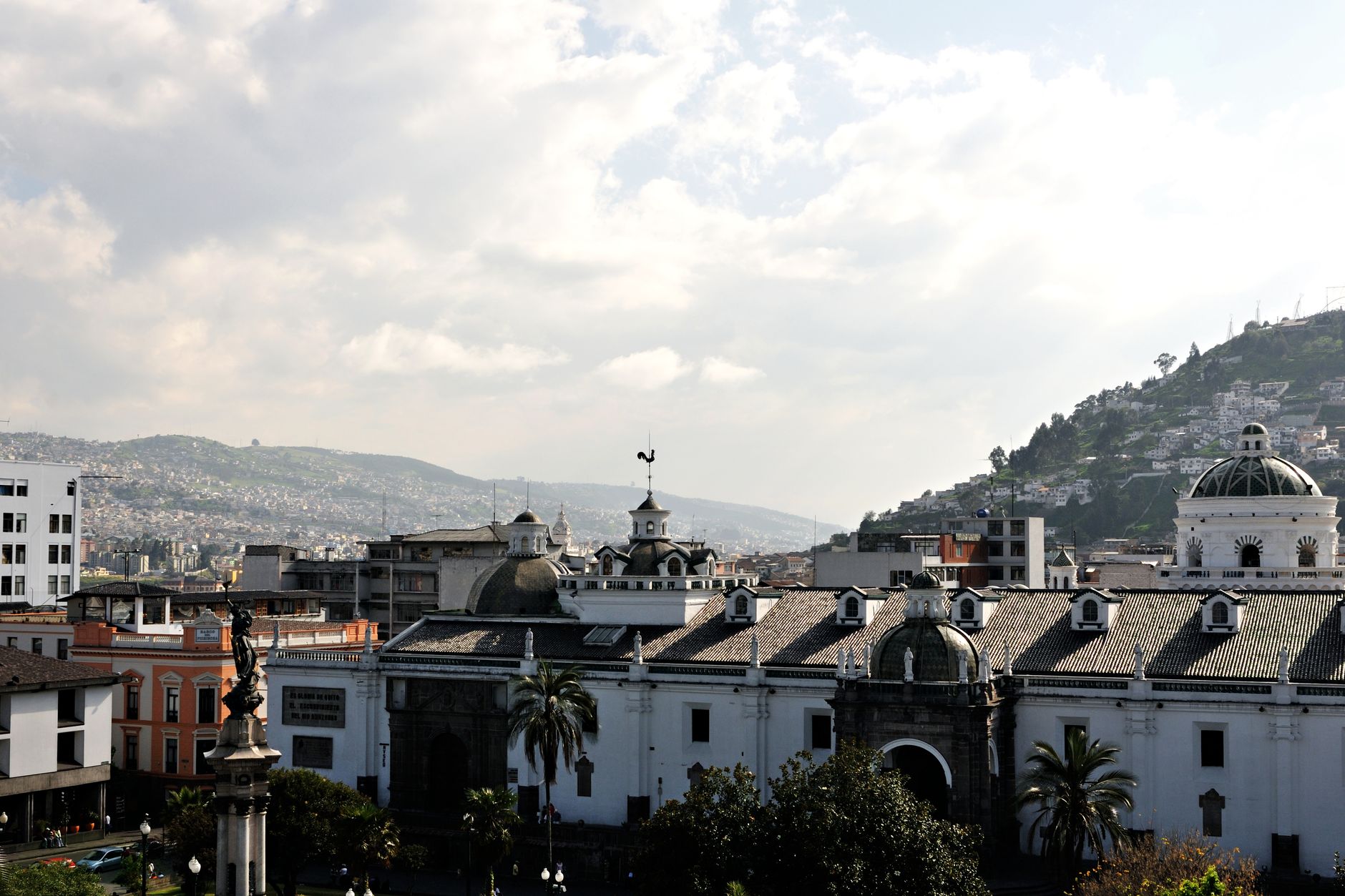 Panoramic view of Quito's colonial architecture and surrounding hills under a cloudy sky.