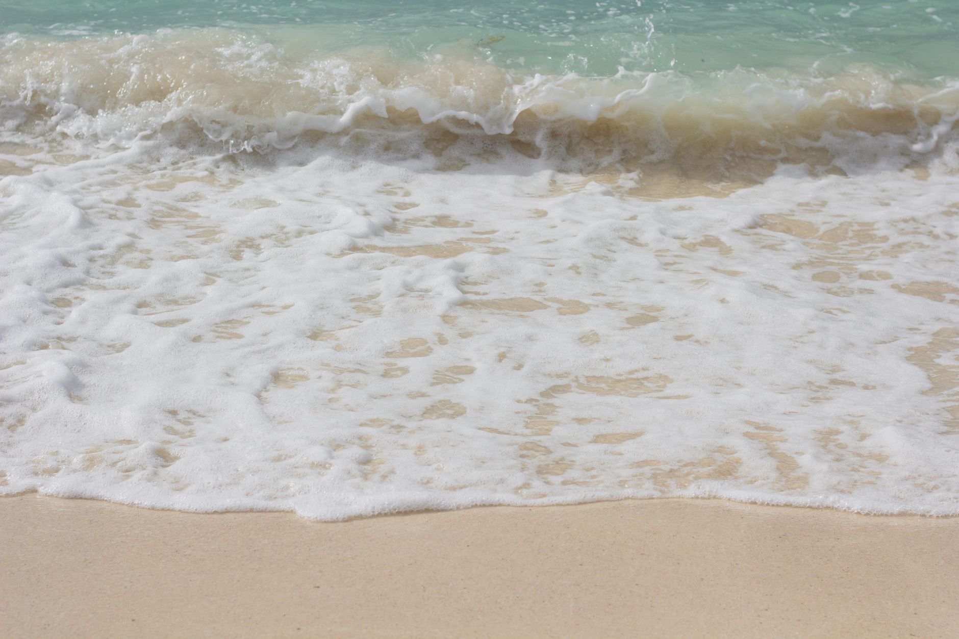 Foamy waves gently caressing the sandy shore at Playa del Carmen, México.
