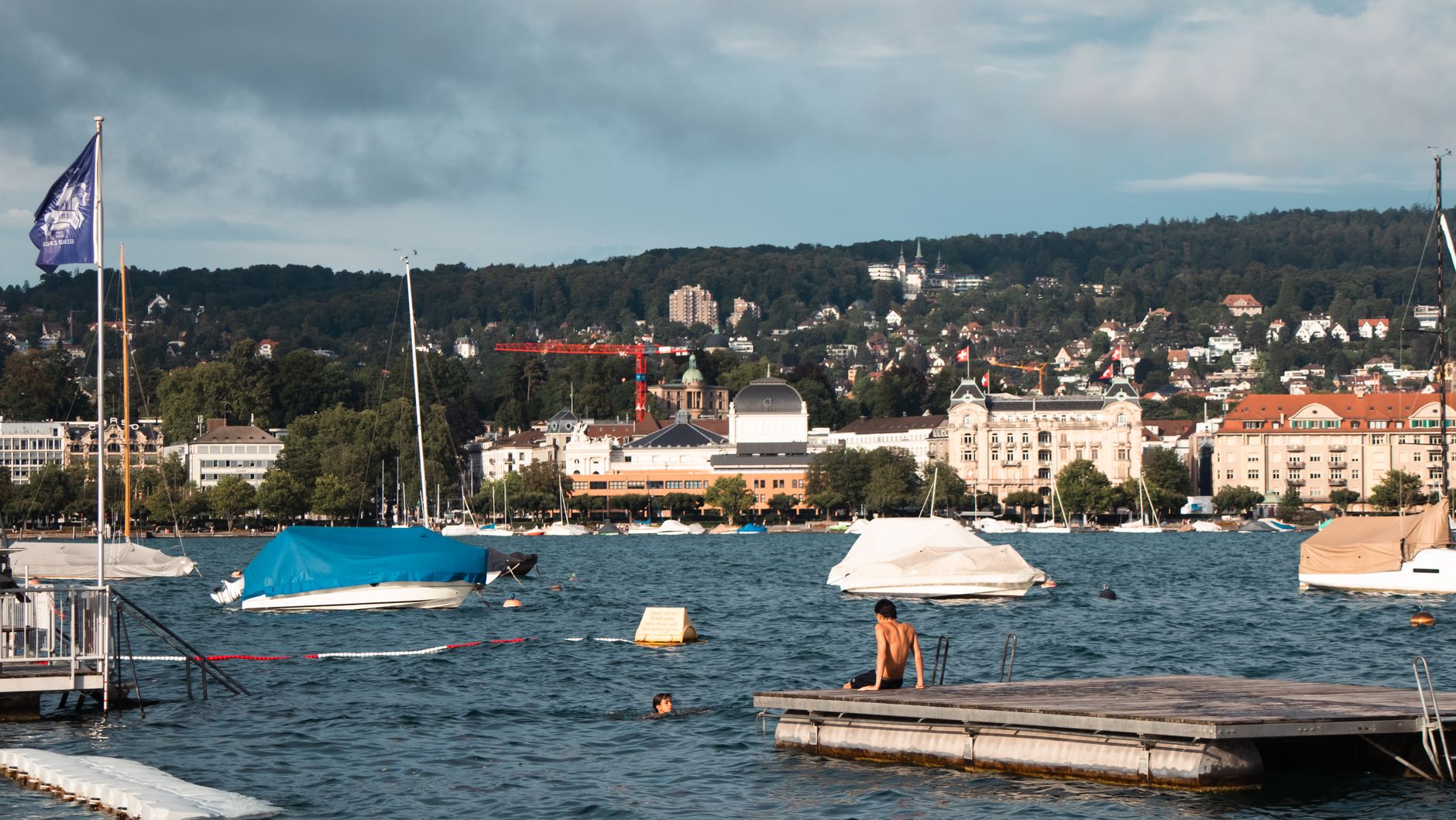 People enjoying a sunny afternoon by Lake Zurich with boats and scenic city backdrop.