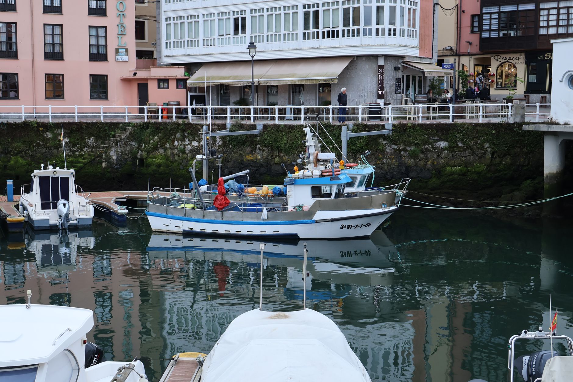 A picturesque view of a fishing boat docked at the harbor in Llanes, Spain, with surrounding buildings.