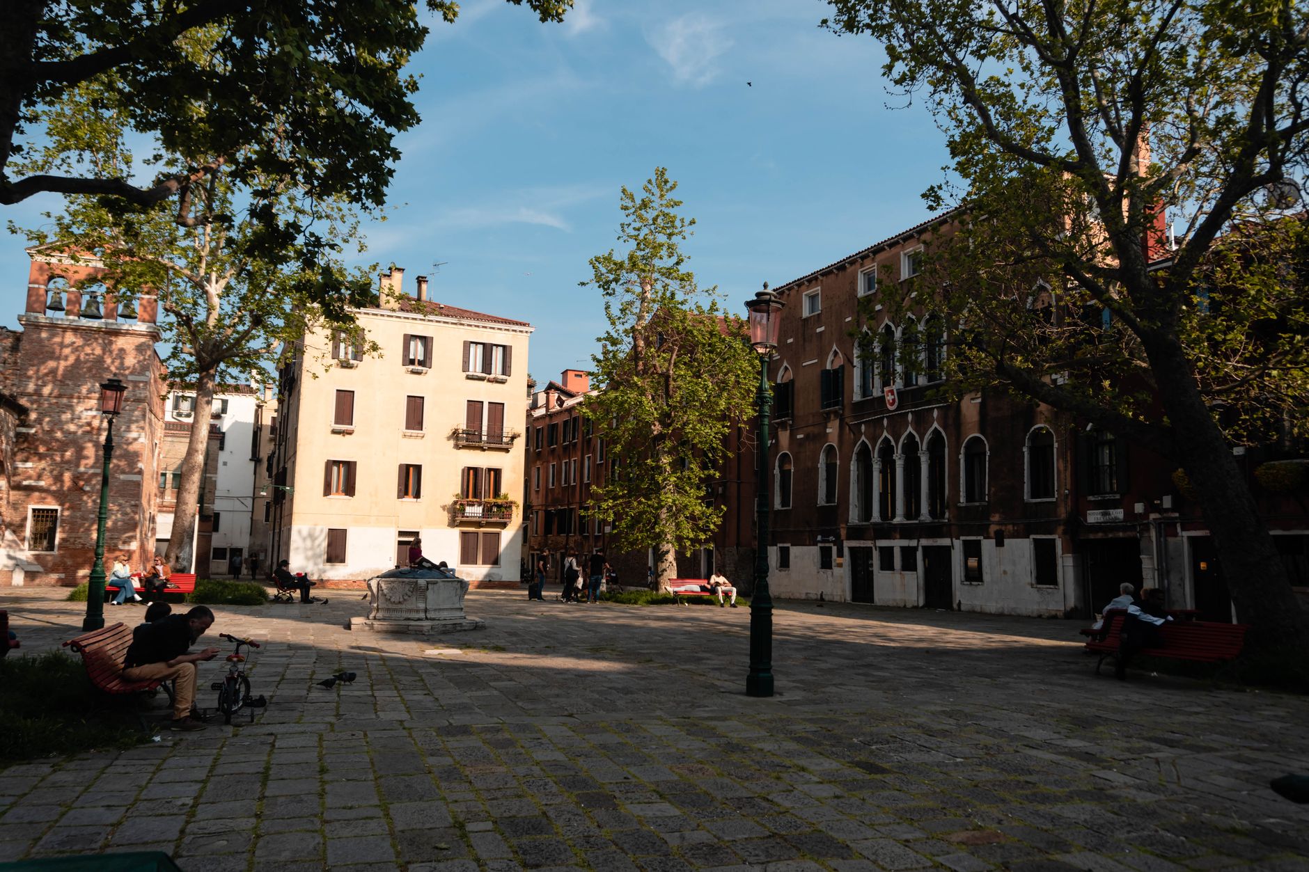 A serene square in Venice, Italy with benches, trees, and historic buildings under a clear blue sky.
