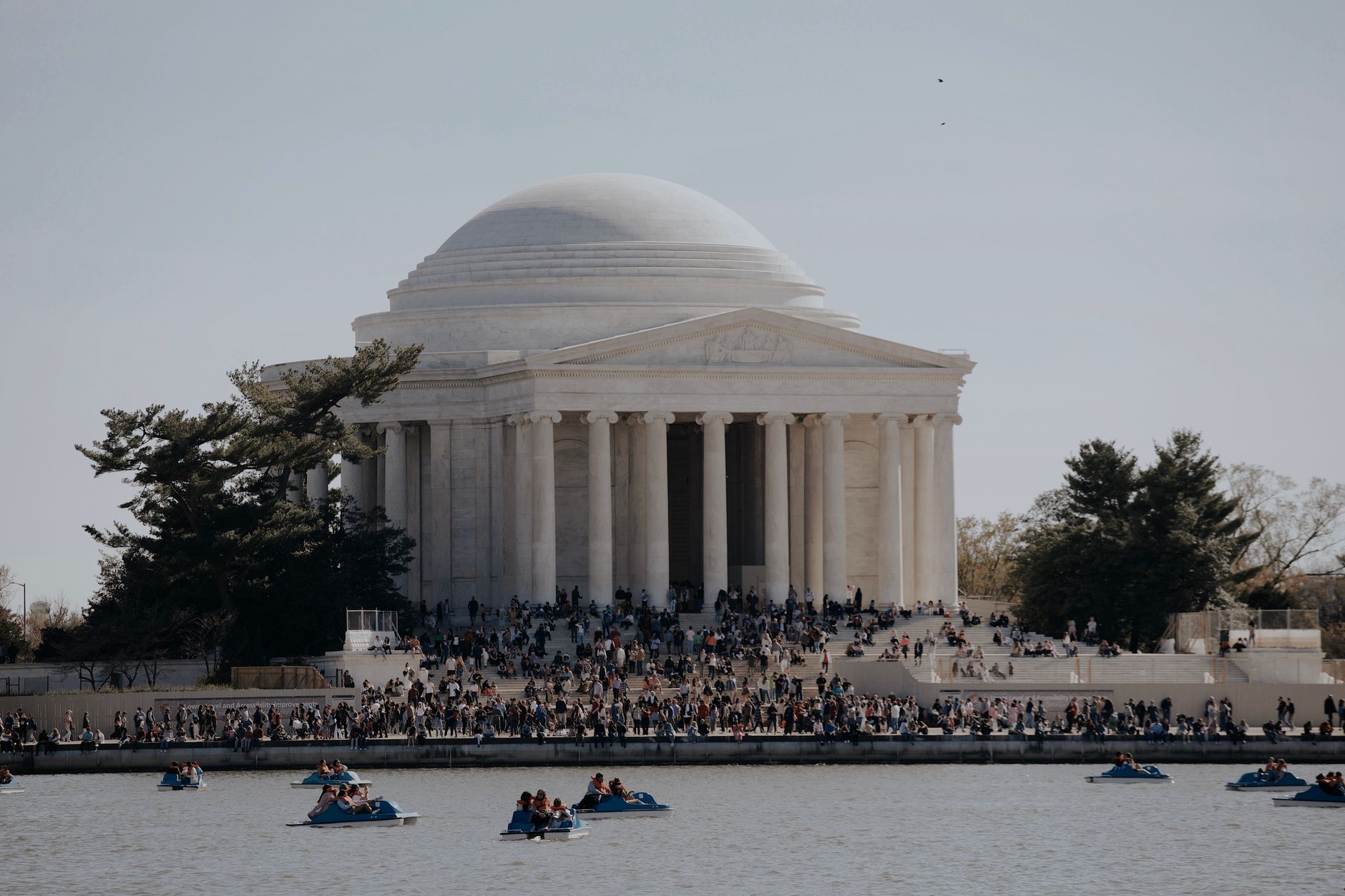 People gather around the Jefferson Memorial on a sunny day, enjoying paddle boating on the river.