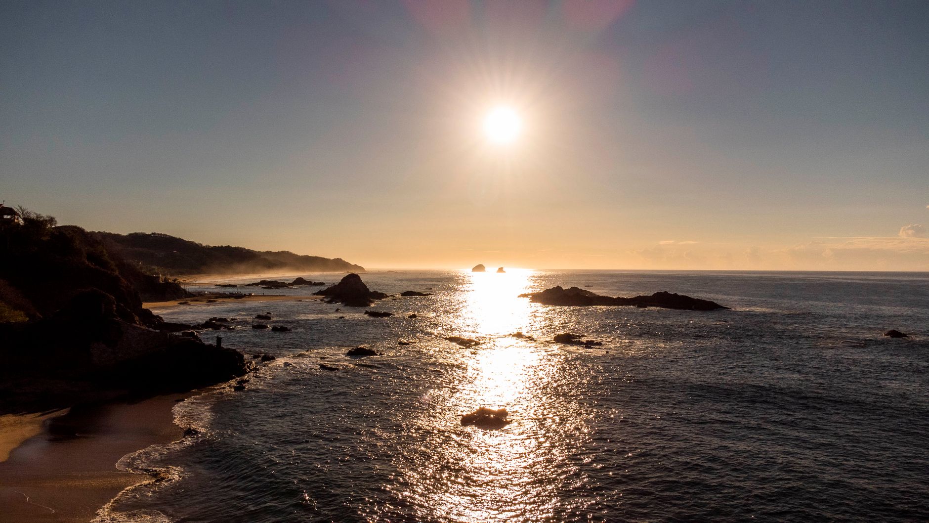Calm ocean scene at sunset in Mazunte, Mexico, with rocky shoreline silhouette.