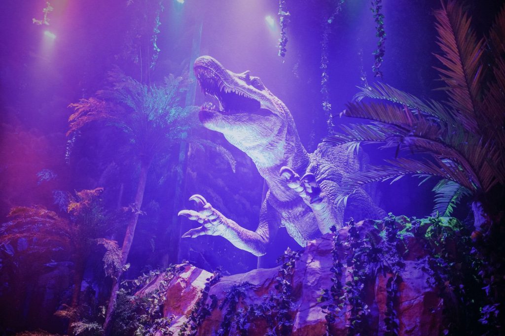 A dinosaur figurine displayed in a jungle setting with vibrant purple lighting and foliage.