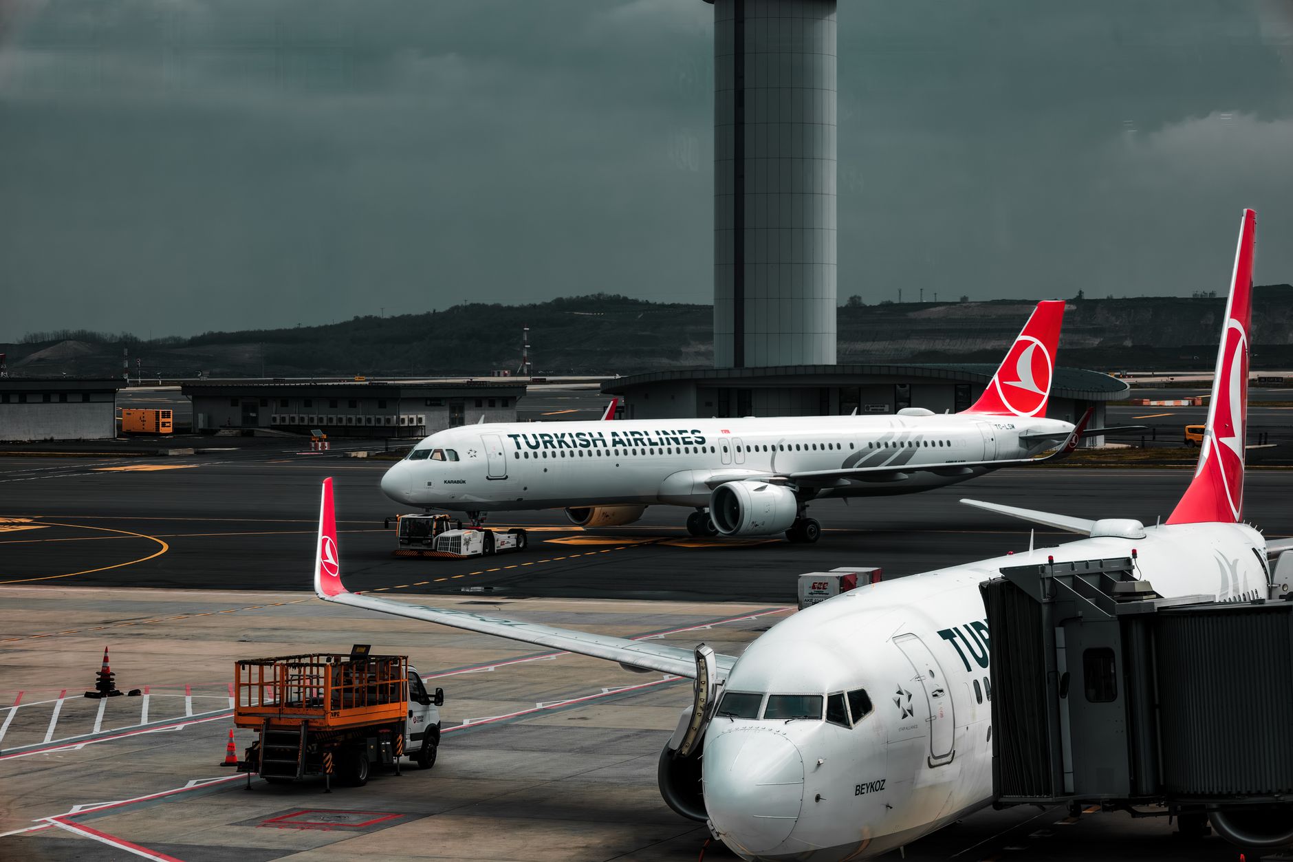 Turkish Airlines planes parked at an airport with a control tower in the background.