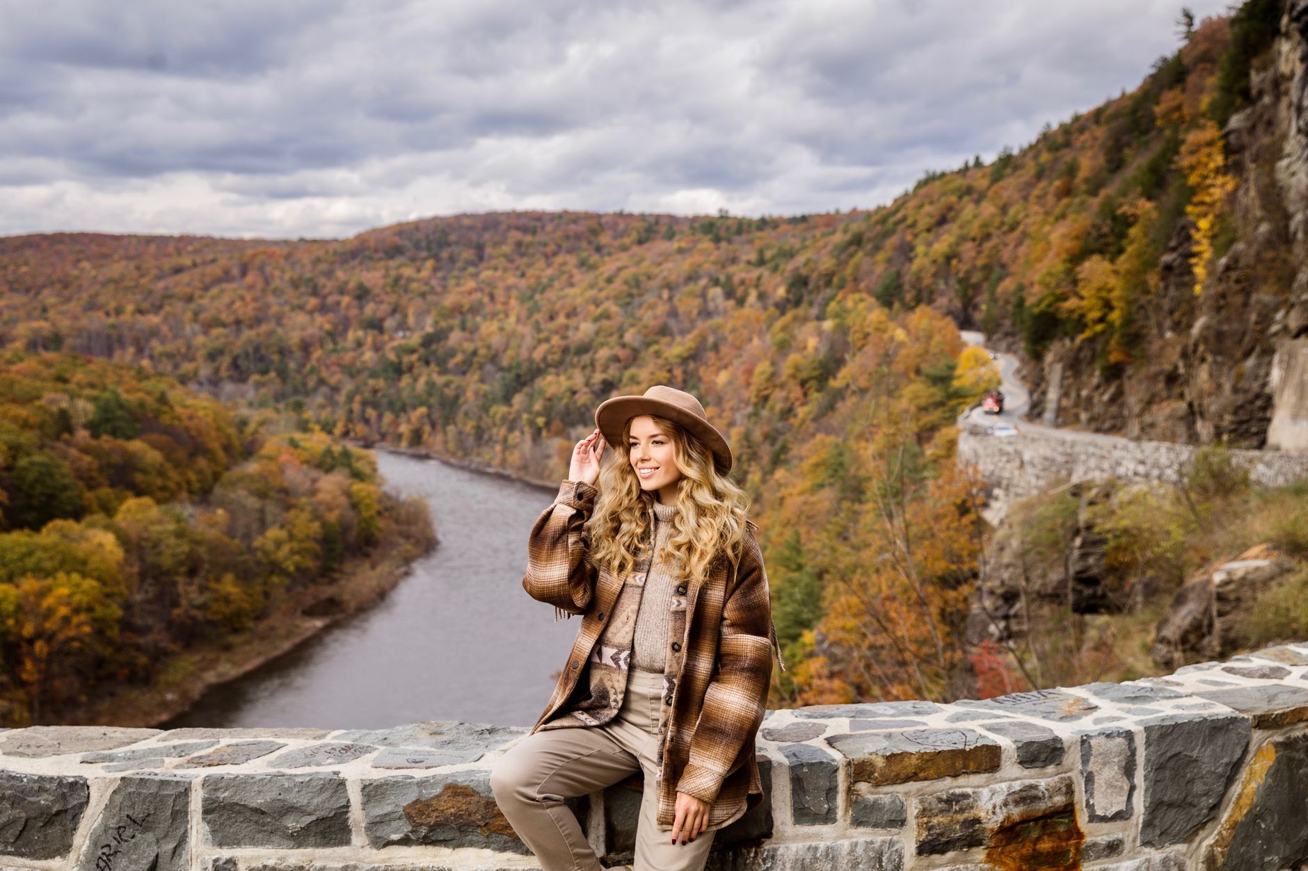Woman in plaid shirt and hat enjoys scenic fall view by the river in Sparrow Bush, NY.