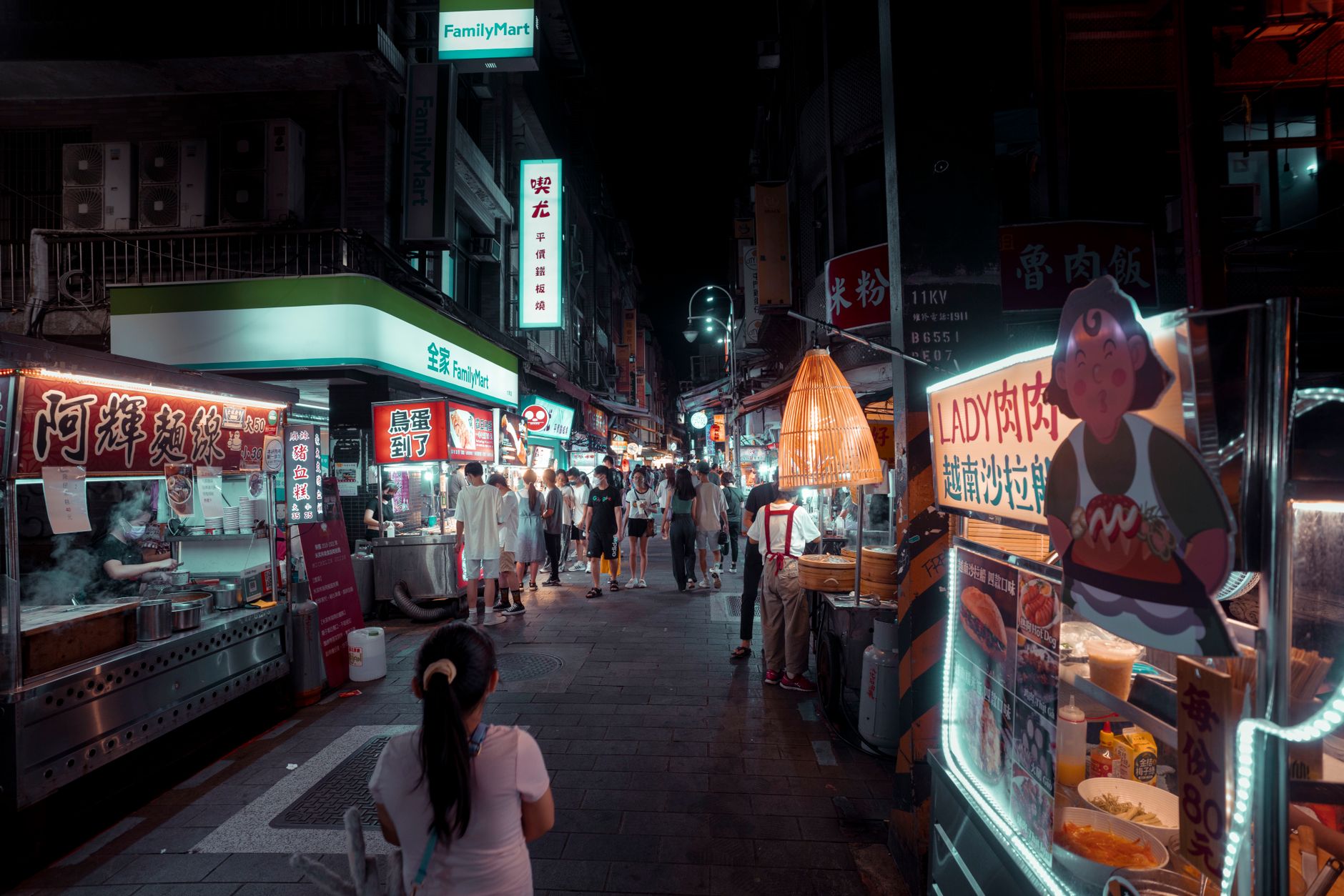 Bustling night market with diverse street food stalls and people shopping under vibrant lights.