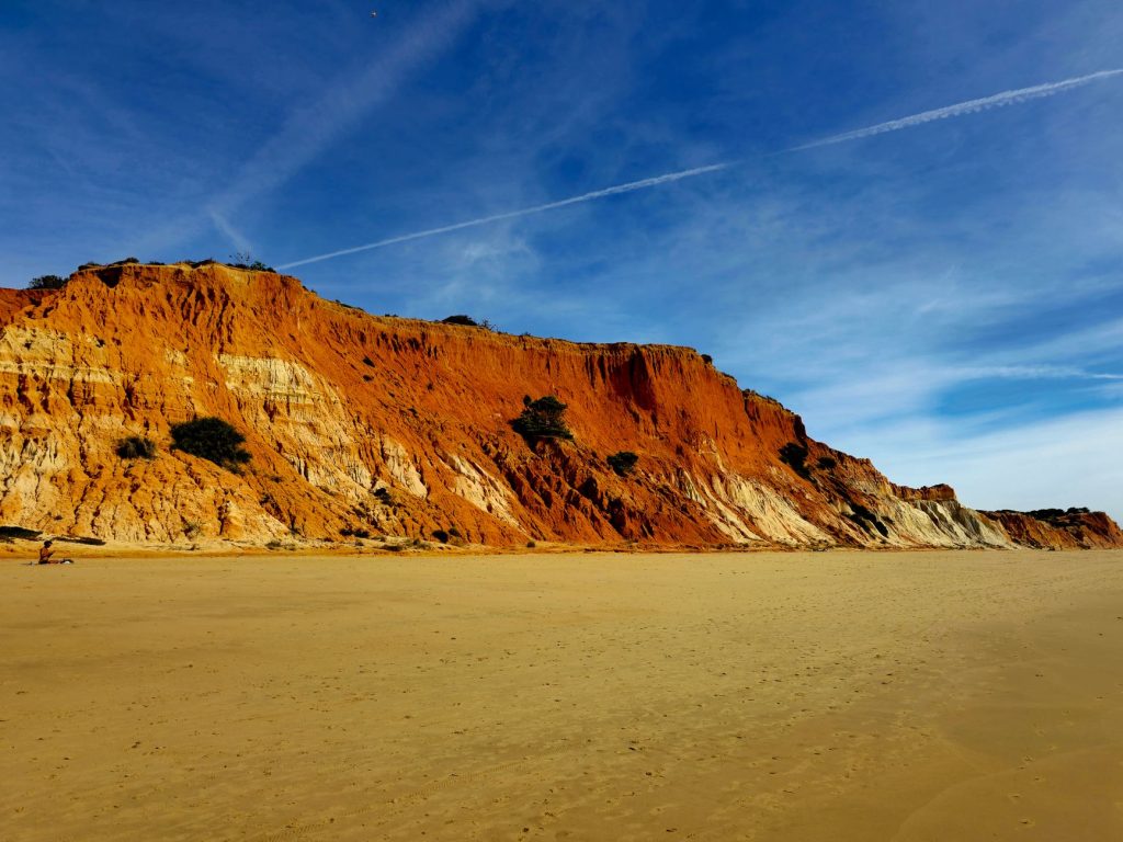 Breathtaking view of Praia da Falésia's red cliffs against a vibrant blue sky in Faro, Portugal.