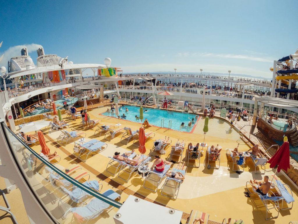 A vibrant scene of people relaxing by a pool on a luxurious cruise ship deck.