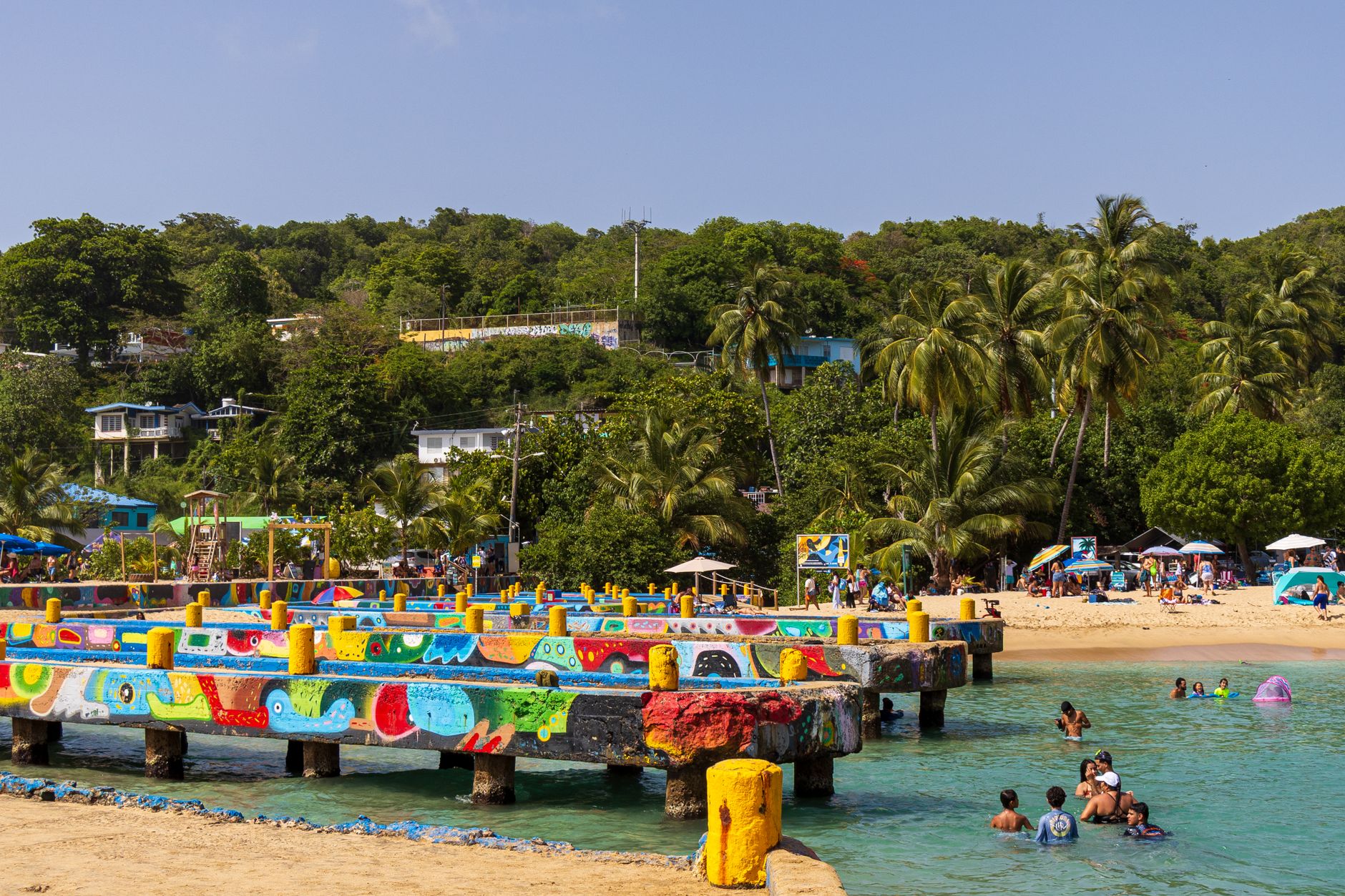 Vibrant beach scene with colorful structures and people enjoying the water in Aguadilla, Puerto Rico.