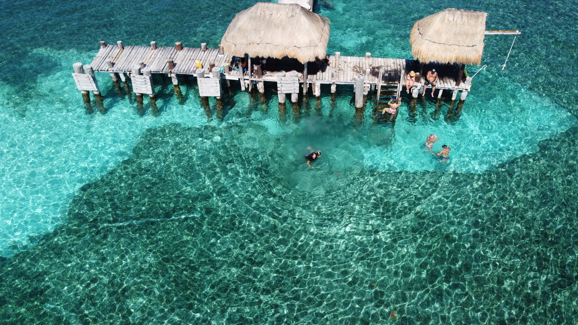 Breathtaking aerial view of Isla Mujeres pier with tourists and clear turquoise waters.