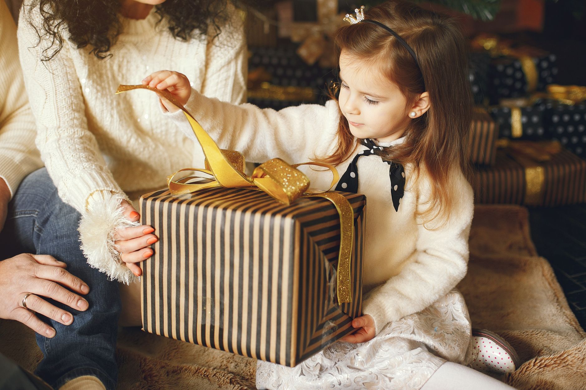 A young girl eagerly opens a beautifully wrapped gift box indoors, capturing a joyful moment.