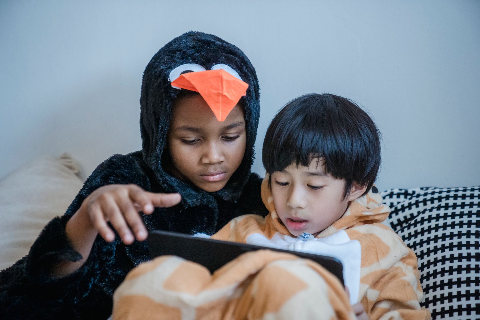 Two children in animal onesies enjoying tablet time in a cozy indoor setting.