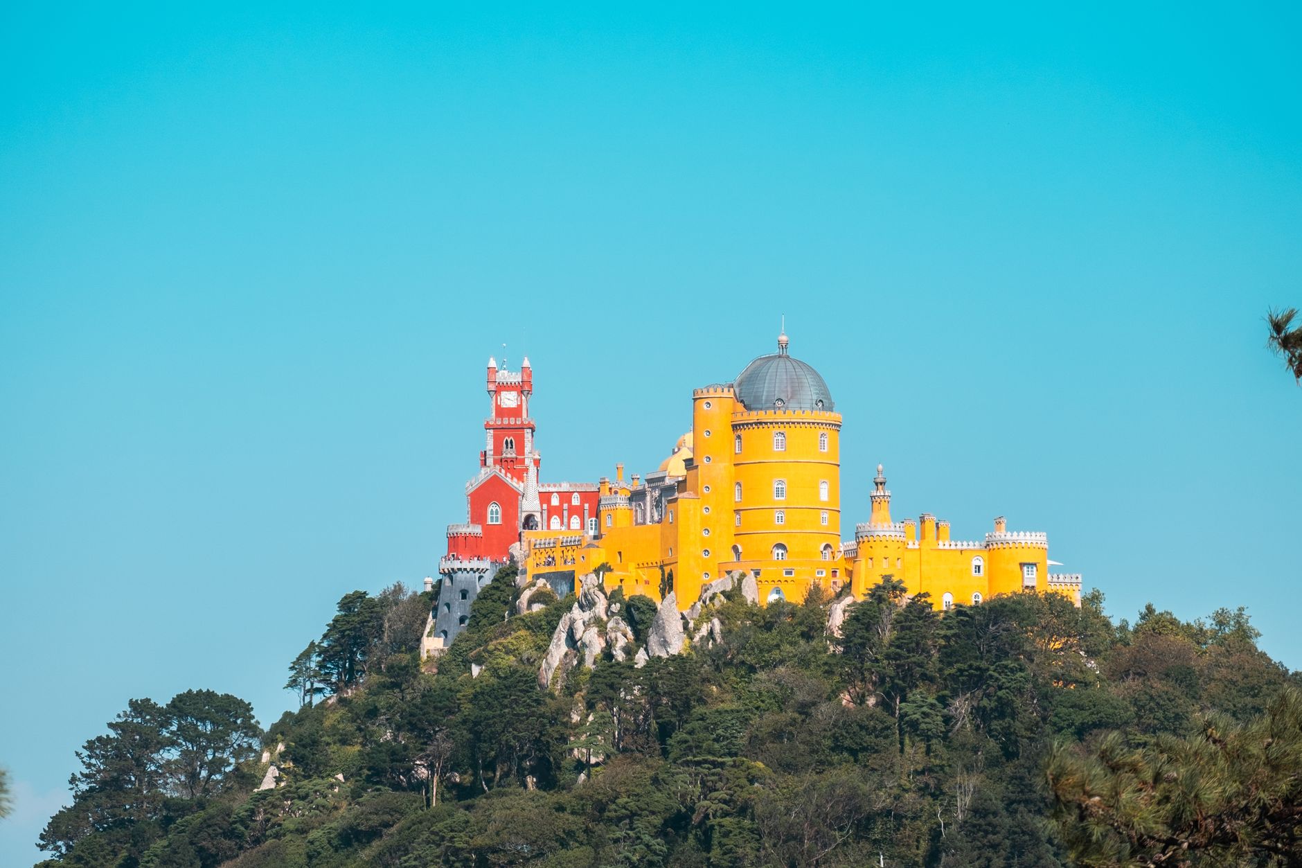 Vibrant Pena Palace on a hilltop in Sintra, Portugal contrasting with a clear blue sky.