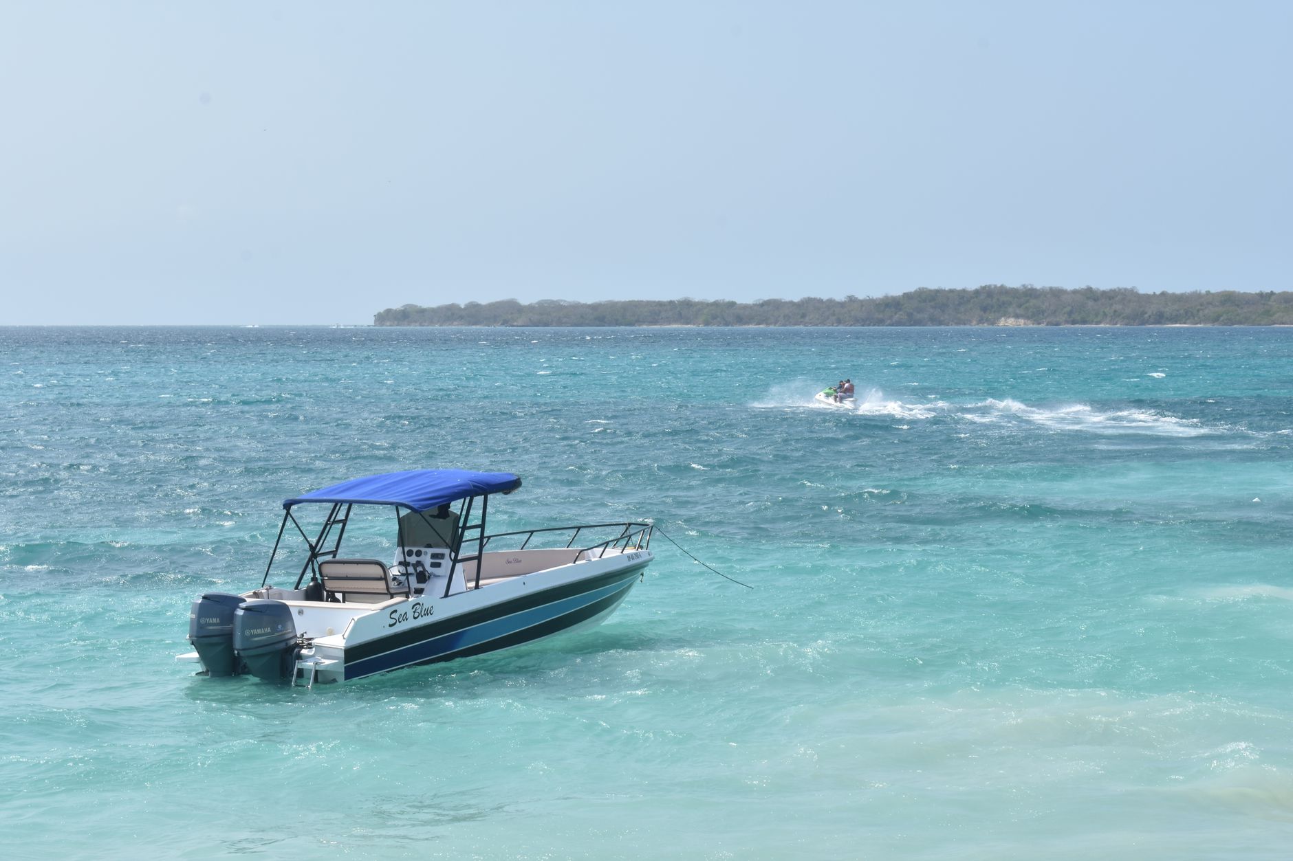 A motorboat floats on the turquoise waters near Cartagena, Colombia, with a backdrop of clear skies and an island.