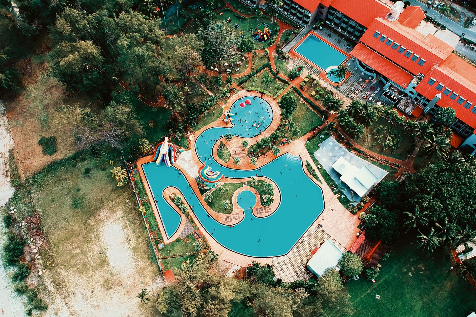 Colorful aerial shot of a resort featuring winding pools and lush gardens, perfect for summer vacations.