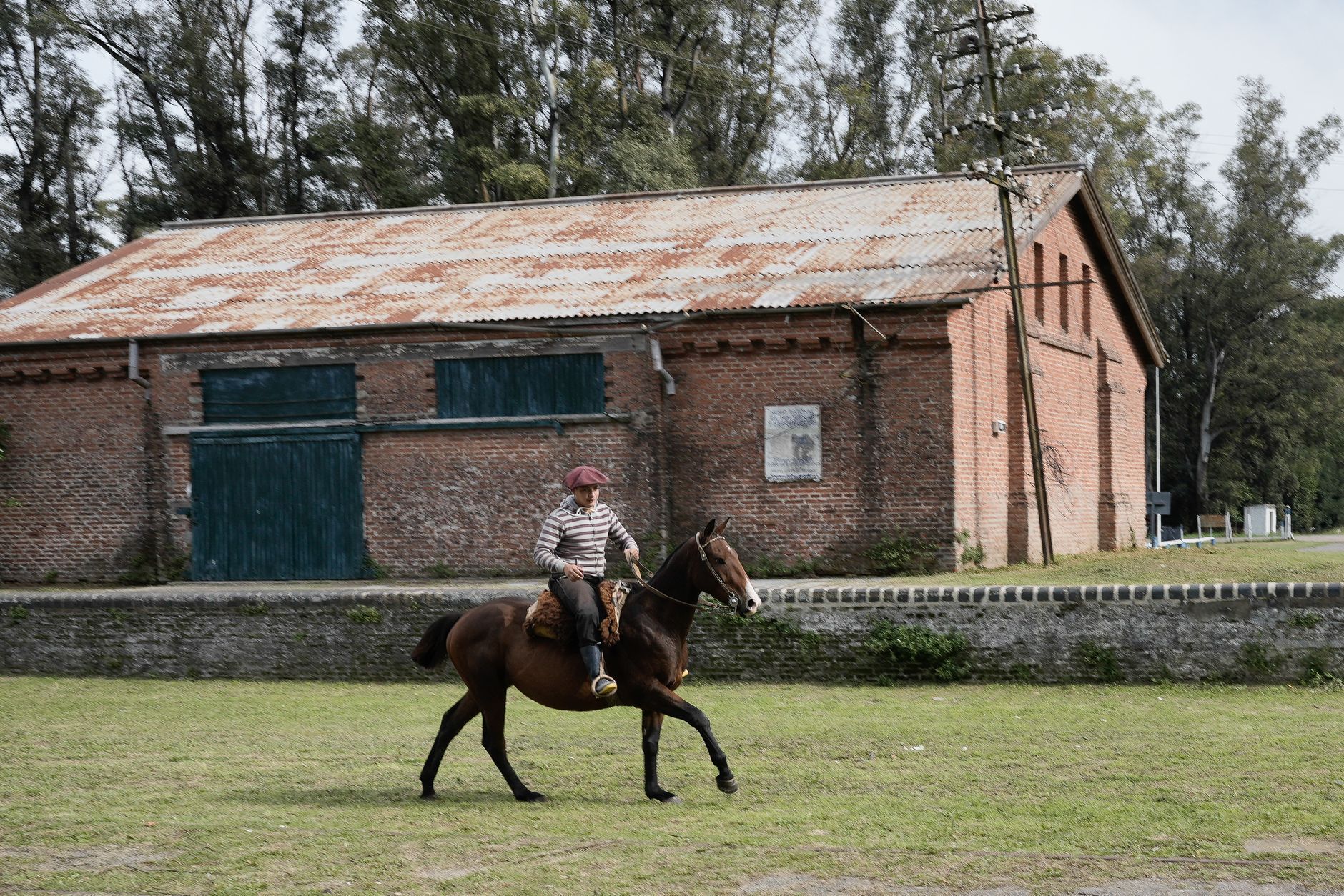 A person riding a horse past a rustic brick building in Uribelarrea, Argentina.
