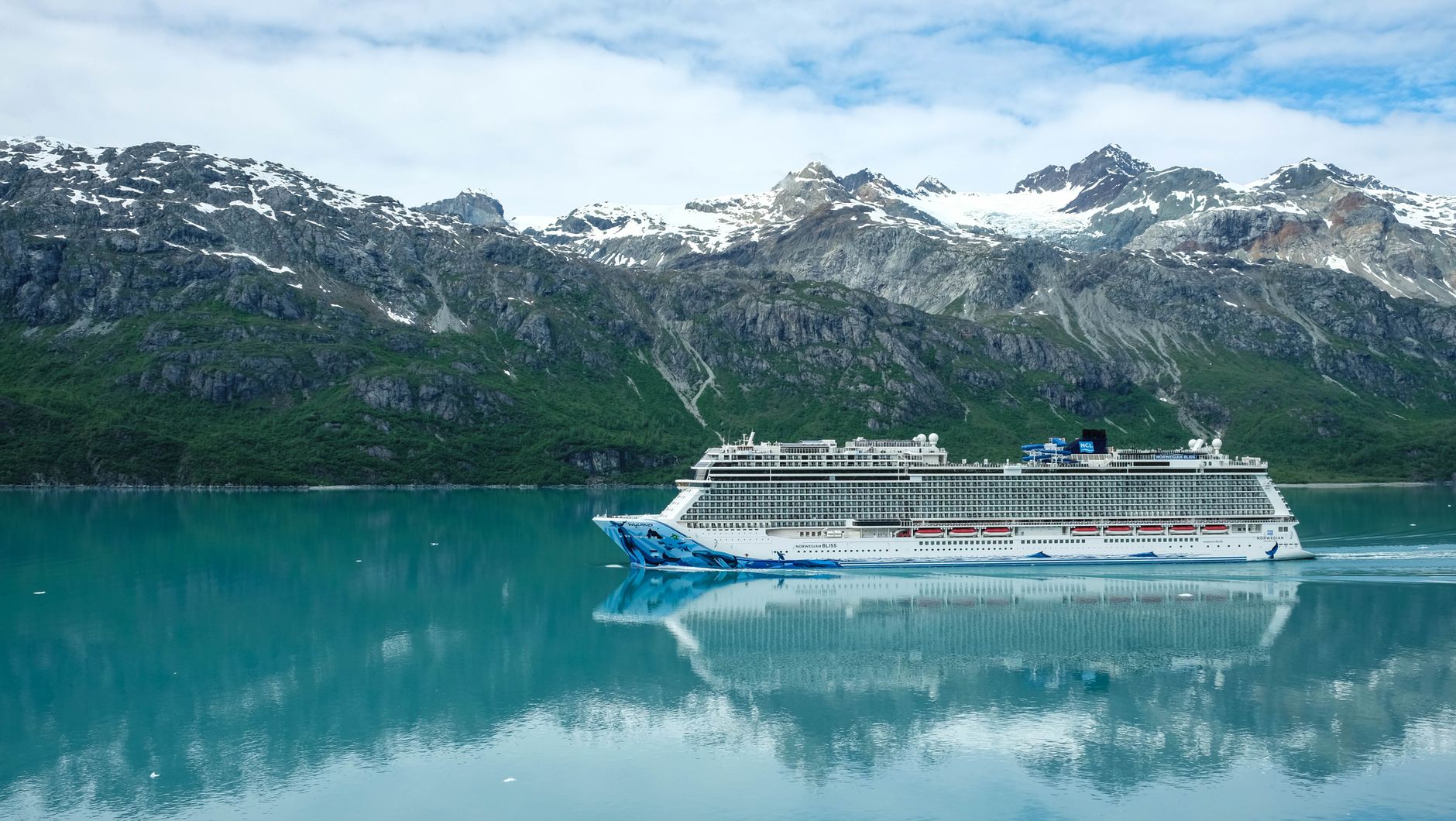 A majestic cruise ship sailing through clear waters with snowy mountains as a backdrop.