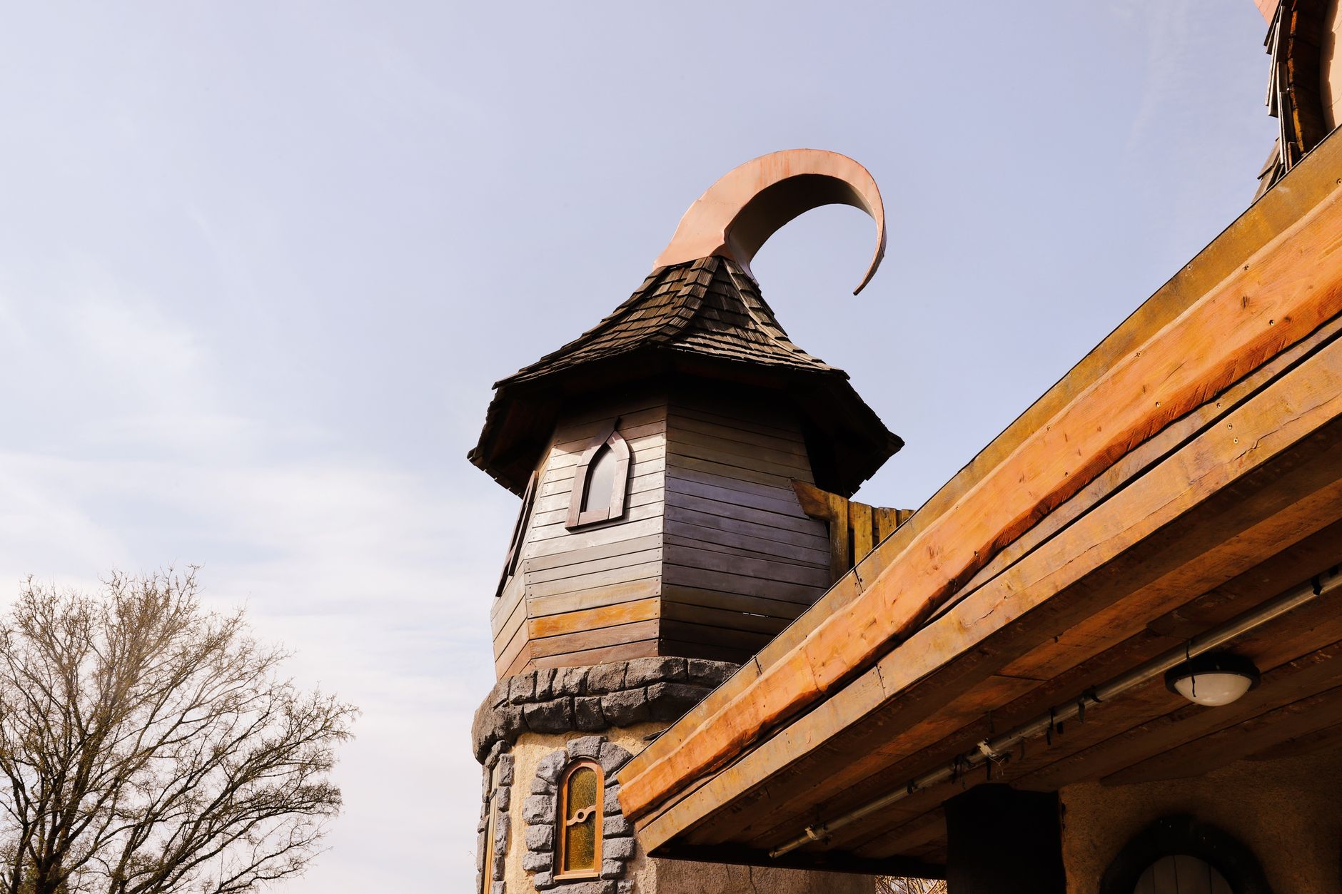 Fairy tale tower with pointed roof and crescent spire, under clear blue skies.