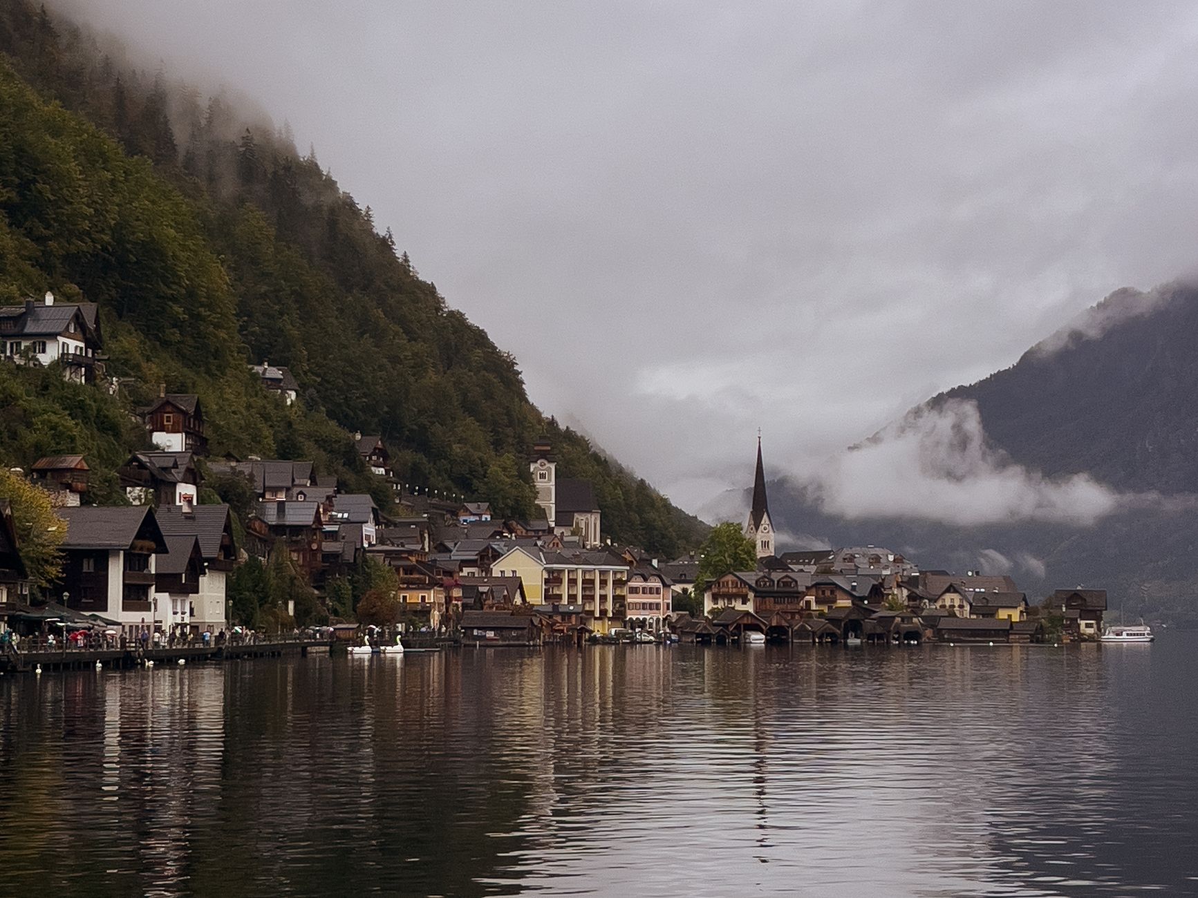 Picturesque village by the lake with misty mountains and charming architecture on a cloudy day.