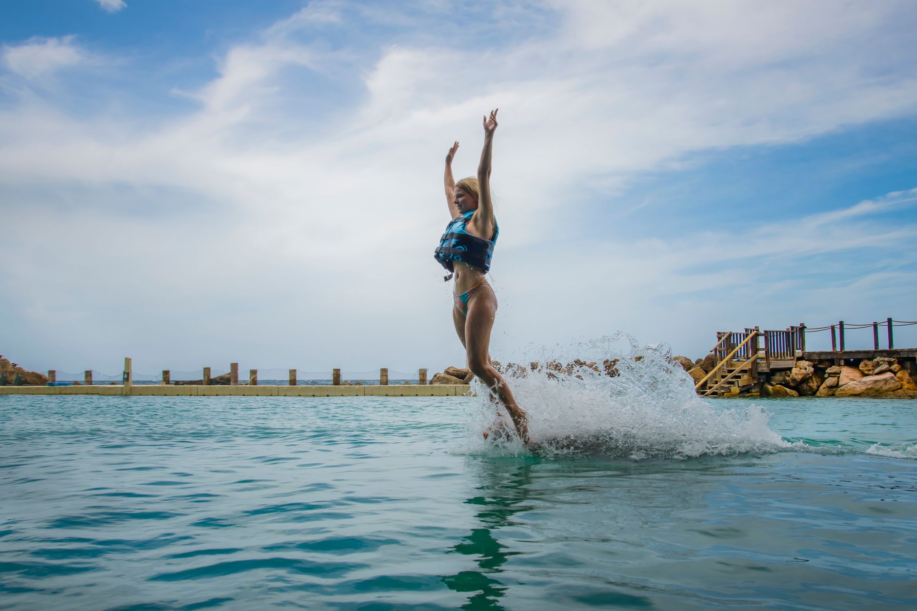 Joyful woman jumps into clear waters at Ocho Rios, creating a splash under a bright sky.