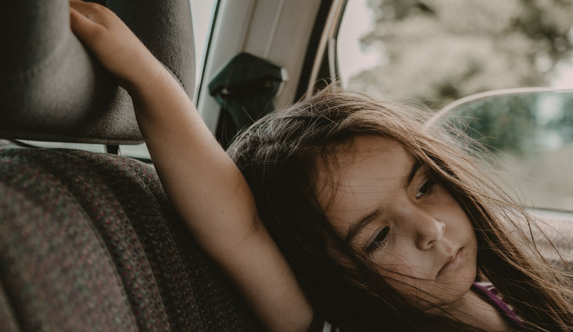 A young girl sits pensively in a car seat, gazing out the window.