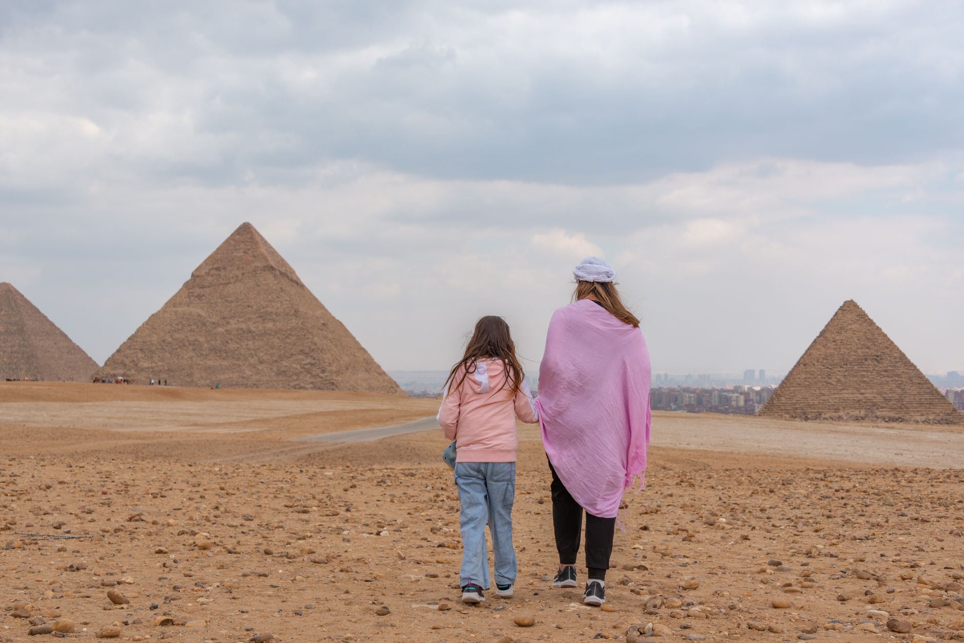 A mother and daughter walk towards the Giza Pyramids, capturing the essence of travel and adventure.