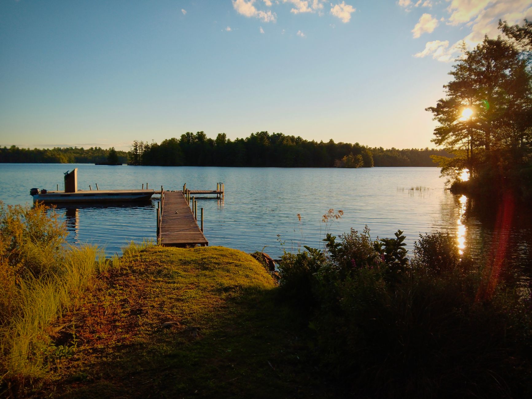 Peaceful lakeside view with a wooden dock, vibrant sunset, and lush trees in Pennsylvania.
