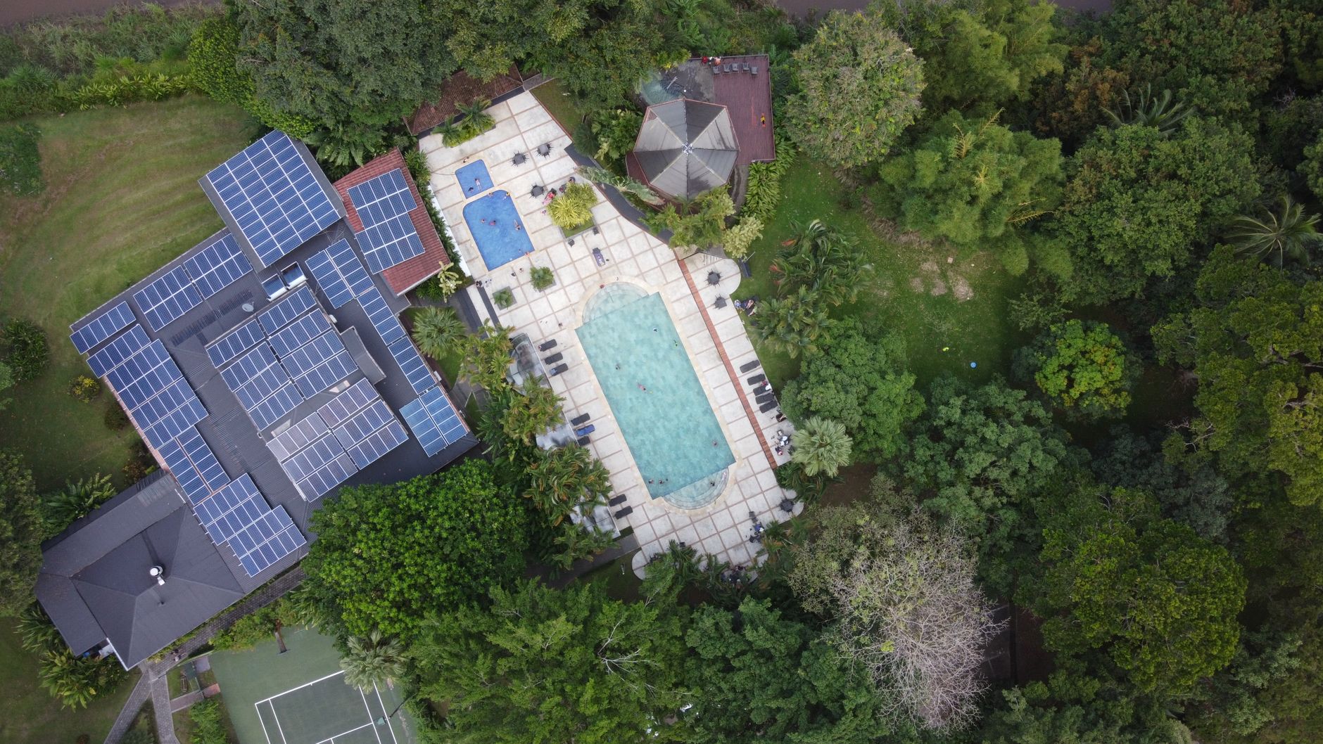 Aerial view of a luxury villa with solar panels and a pool in vibrant green surroundings.