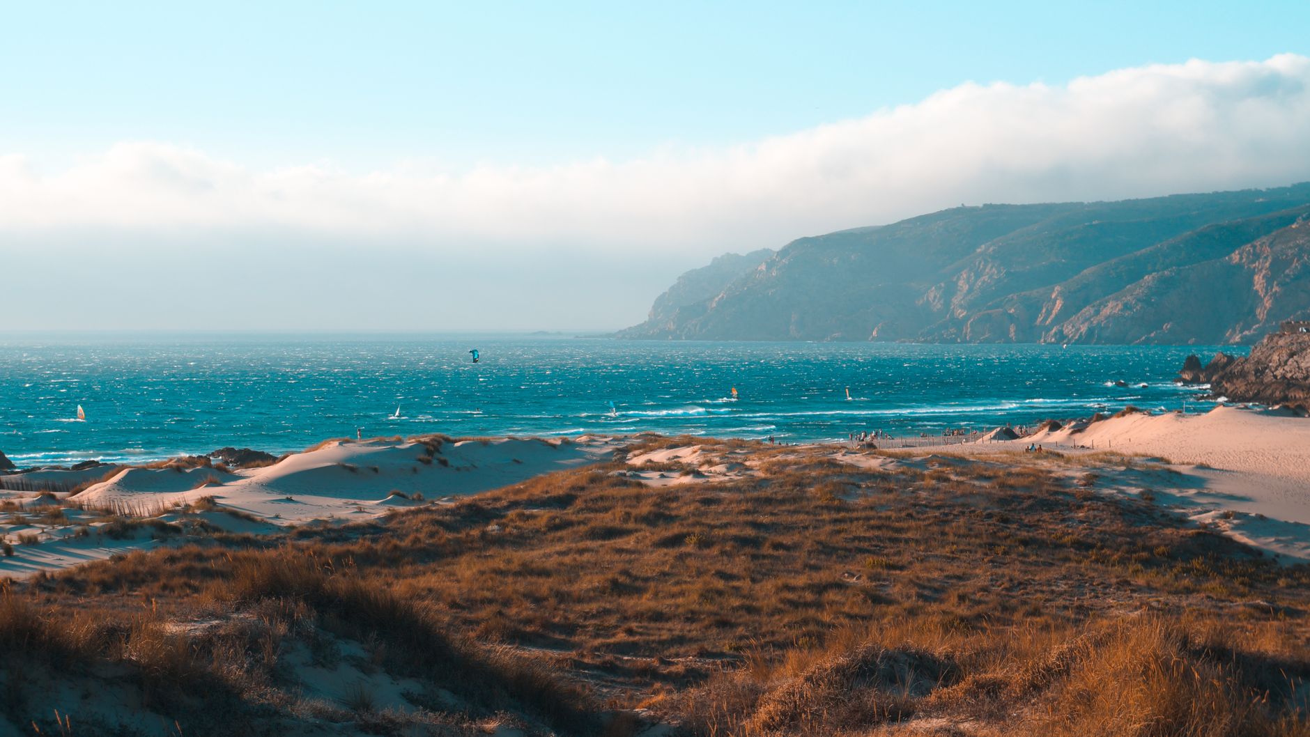Picturesque view of bright sea with horizon line and rippled water near mounts and uneven terrain with faded grass under blue cloudy sky in daylight