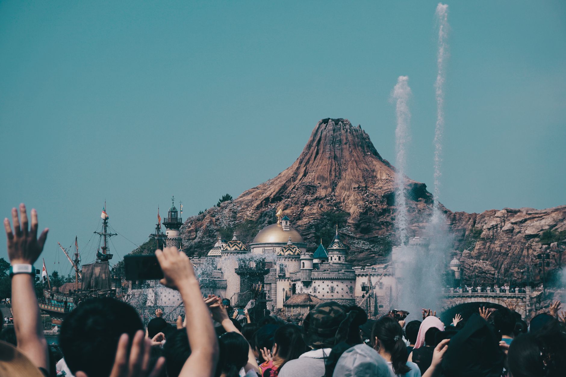 Vibrant theme park scene with a crowd near a volcano and dome during the day.