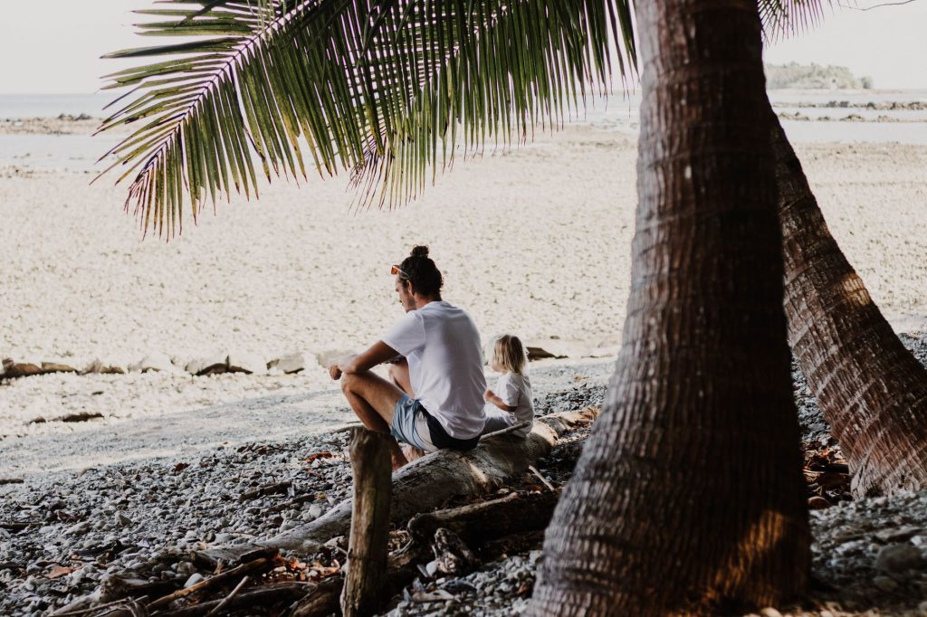 Man and child relax on a serene beach in Costa Rica under palm trees.