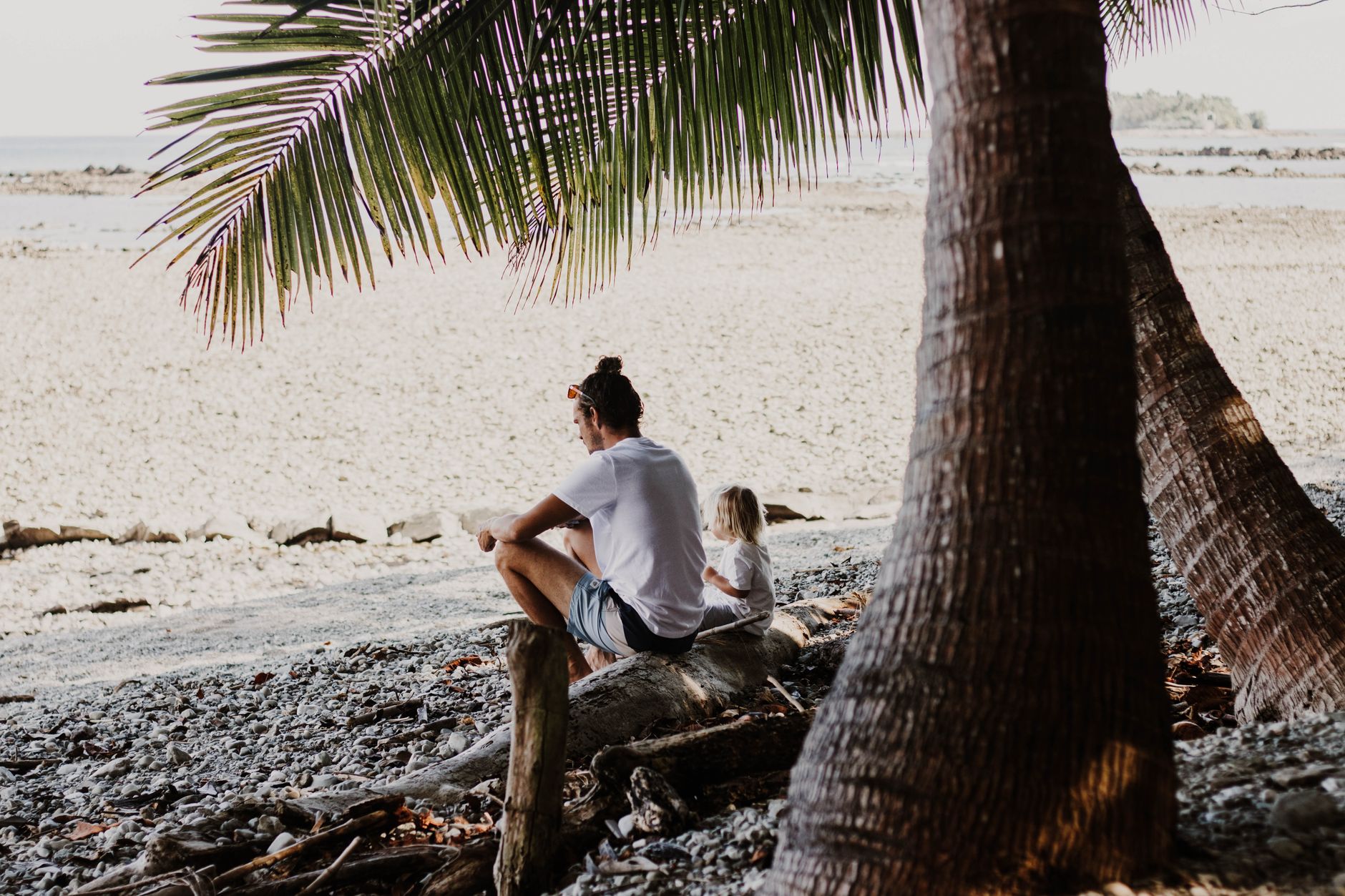 Man and child relax on a serene beach in Costa Rica under palm trees.