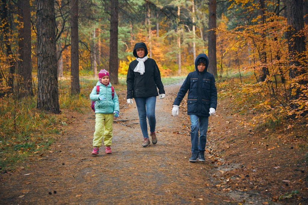 A mother and her two children walking in a vibrant autumn forest, enjoying nature together.