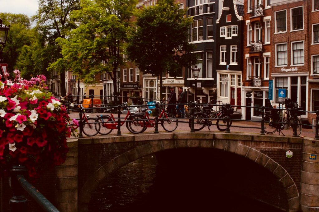 Scenic view of an Amsterdam canal bridge adorned with bicycles and vibrant flowers, perfect for urban travel inspiration.
